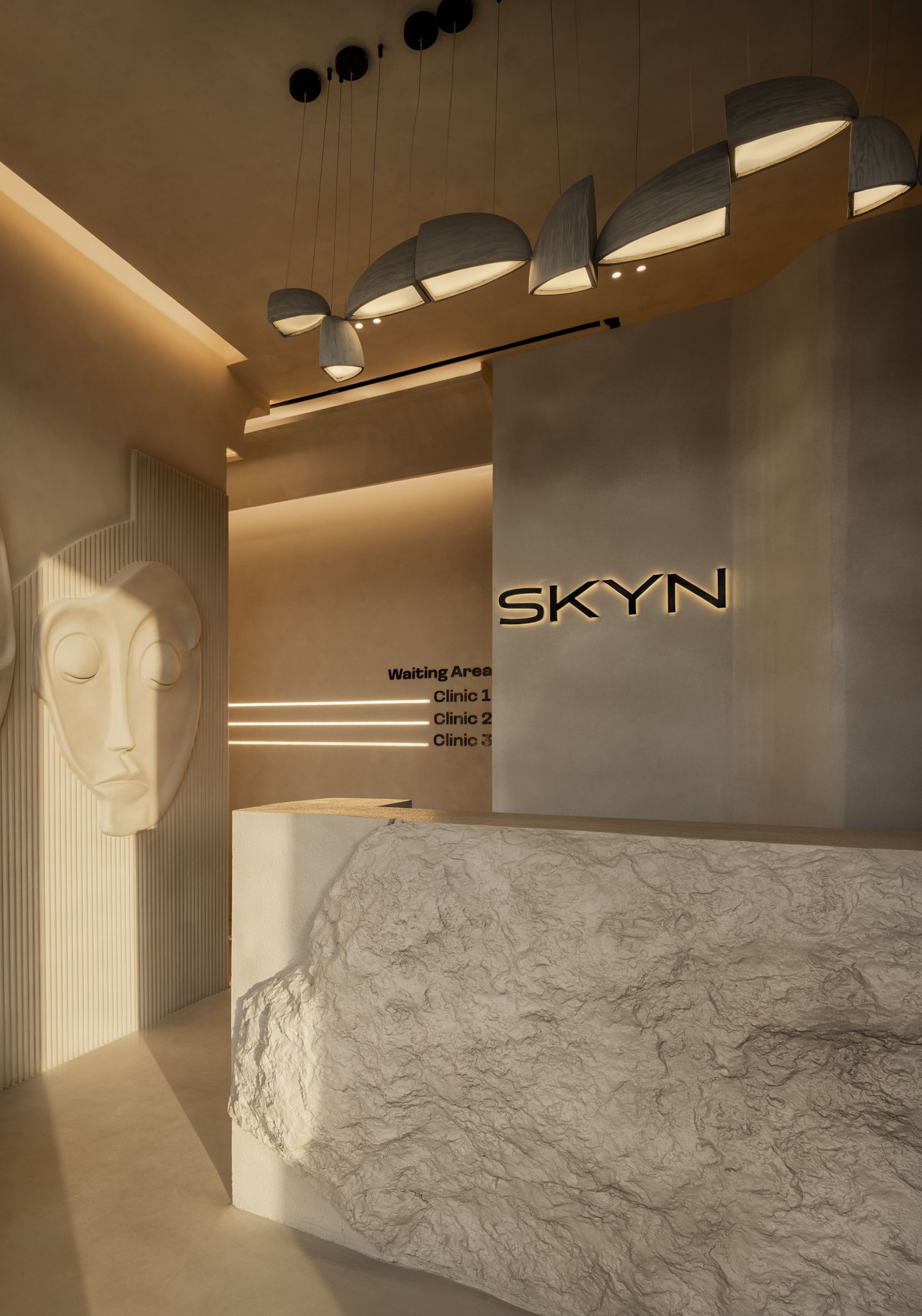 Elegant SKYN clinic reception desk made of raw marble with sculptural pendant lights and a decorative face sculpture.