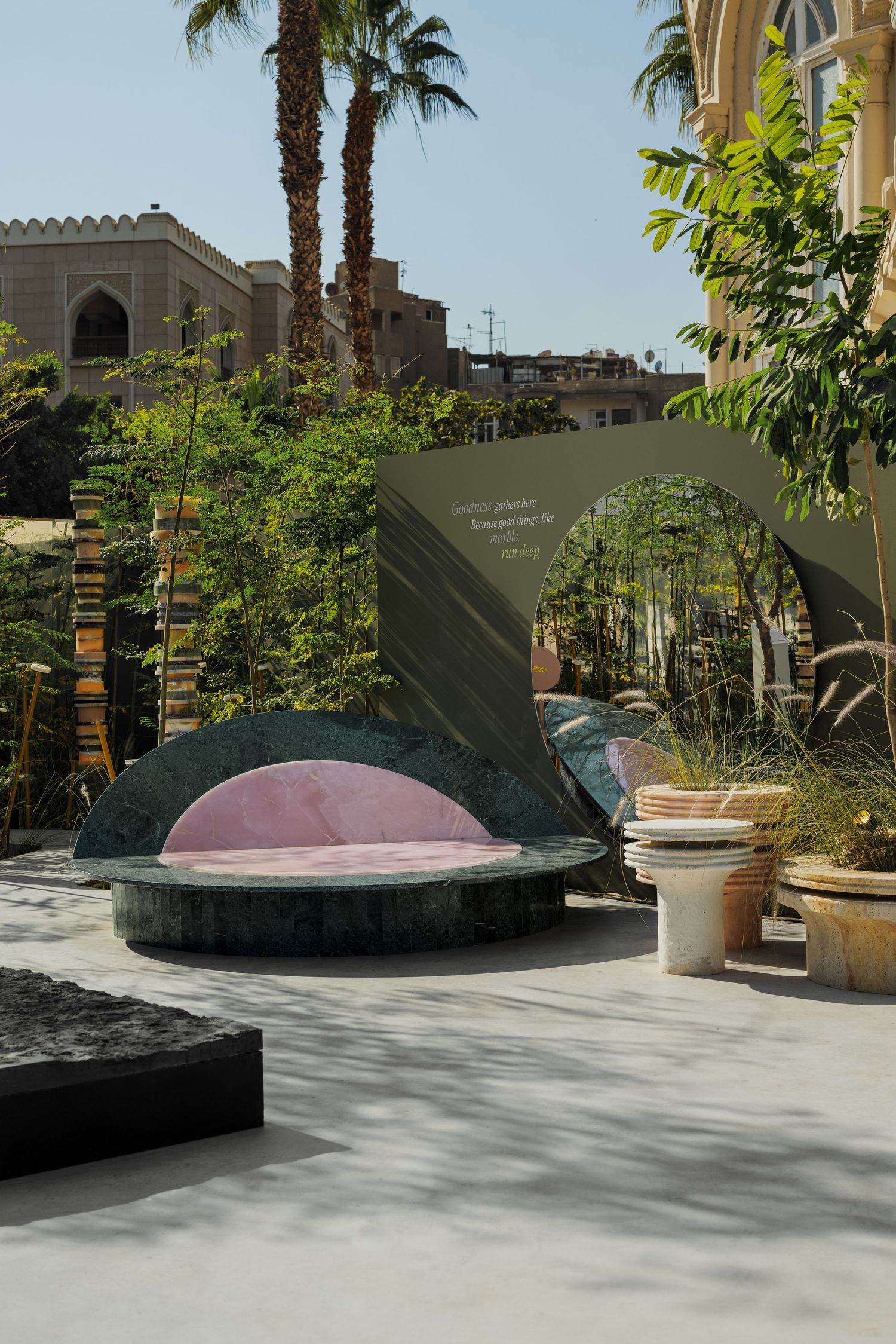 Outdoor garden installation with green marble daybed and pink cushion surrounded by lush plants.