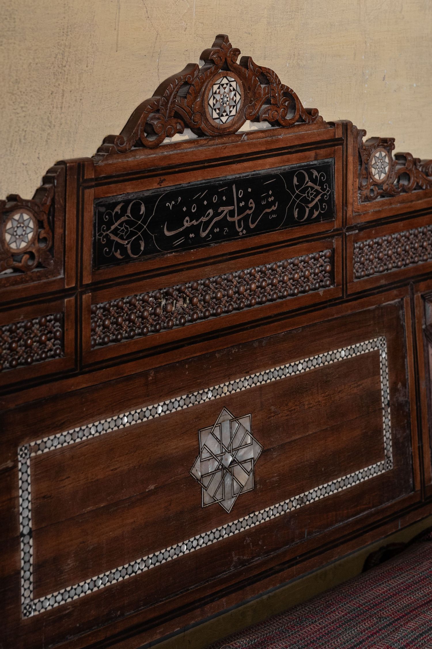 Ornate Arabic carved wooden headboard with mother-of-pearl inlay and intricate geometric Islamic patterns.