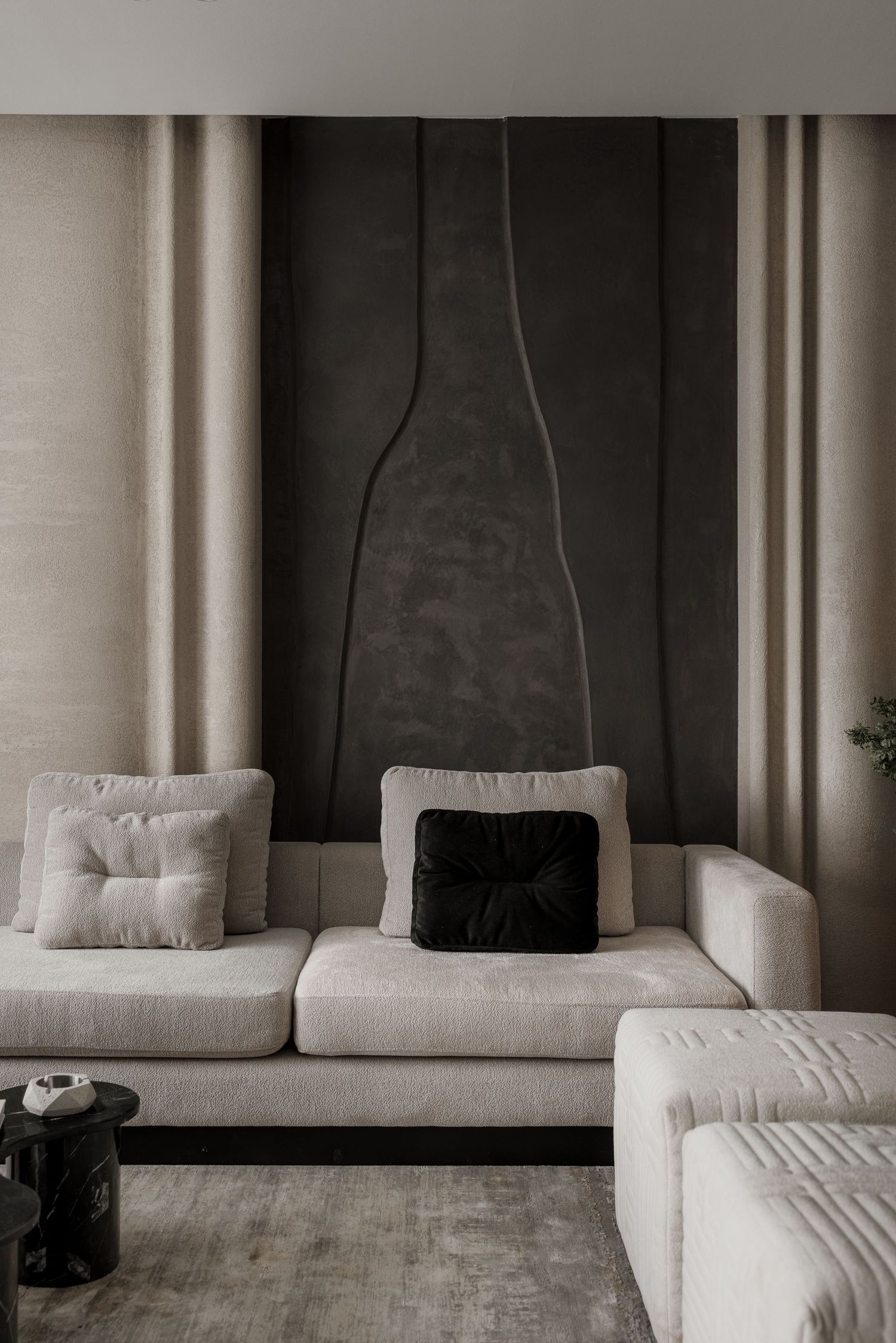 Luxurious beige modular sofa with mixed cushions against a dark textured wall panel in a modern living room.