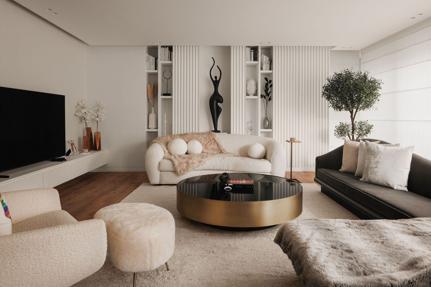 Contemporary living room with cream bouclé sofa, gold coffee table, black figurine sculpture, and built-in shelving.