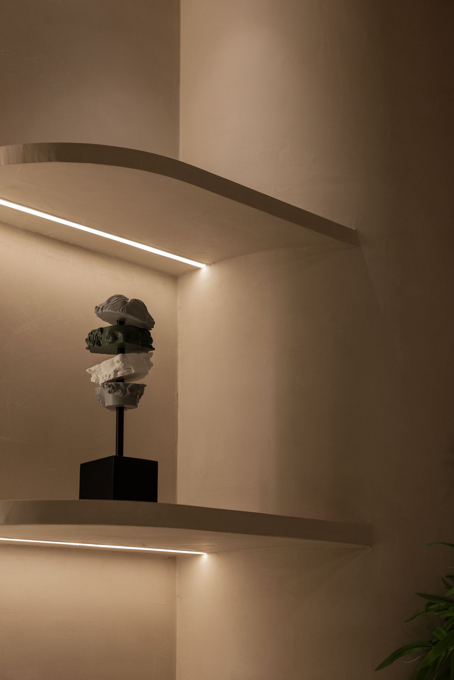 Minimalist illuminated floating shelves with LED strip lighting displaying a stacked stone sculpture on a black pedestal.