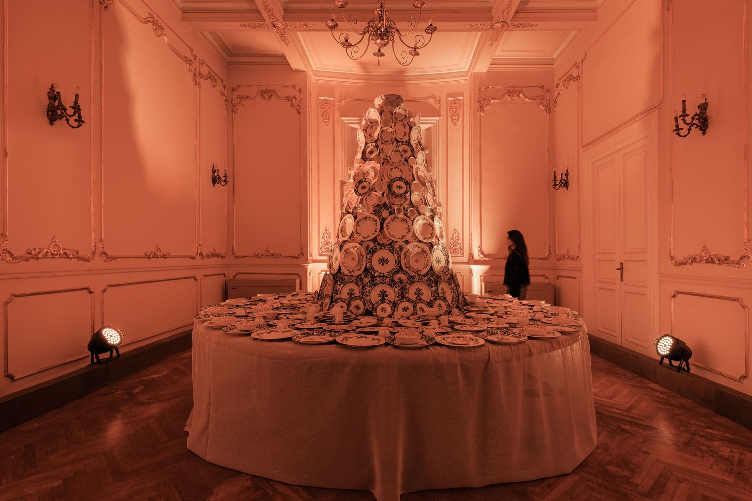 Large pyramid-shaped tower of decorative china plates on a round table in an elegant warmly lit room.