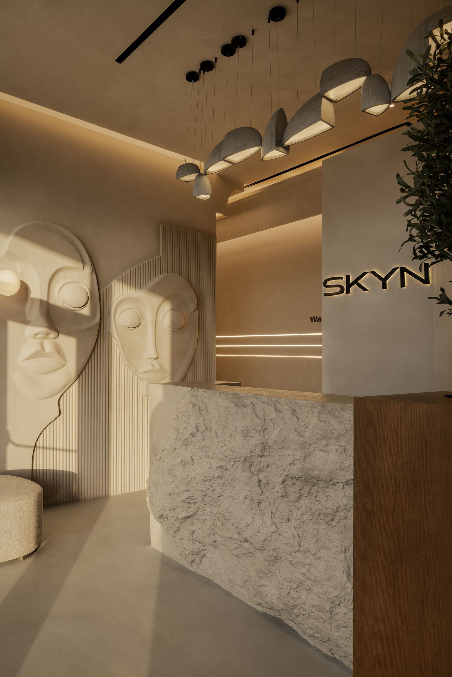 Modern minimalist SKYN reception with marble desk, sculptural face art, and warm lighting.