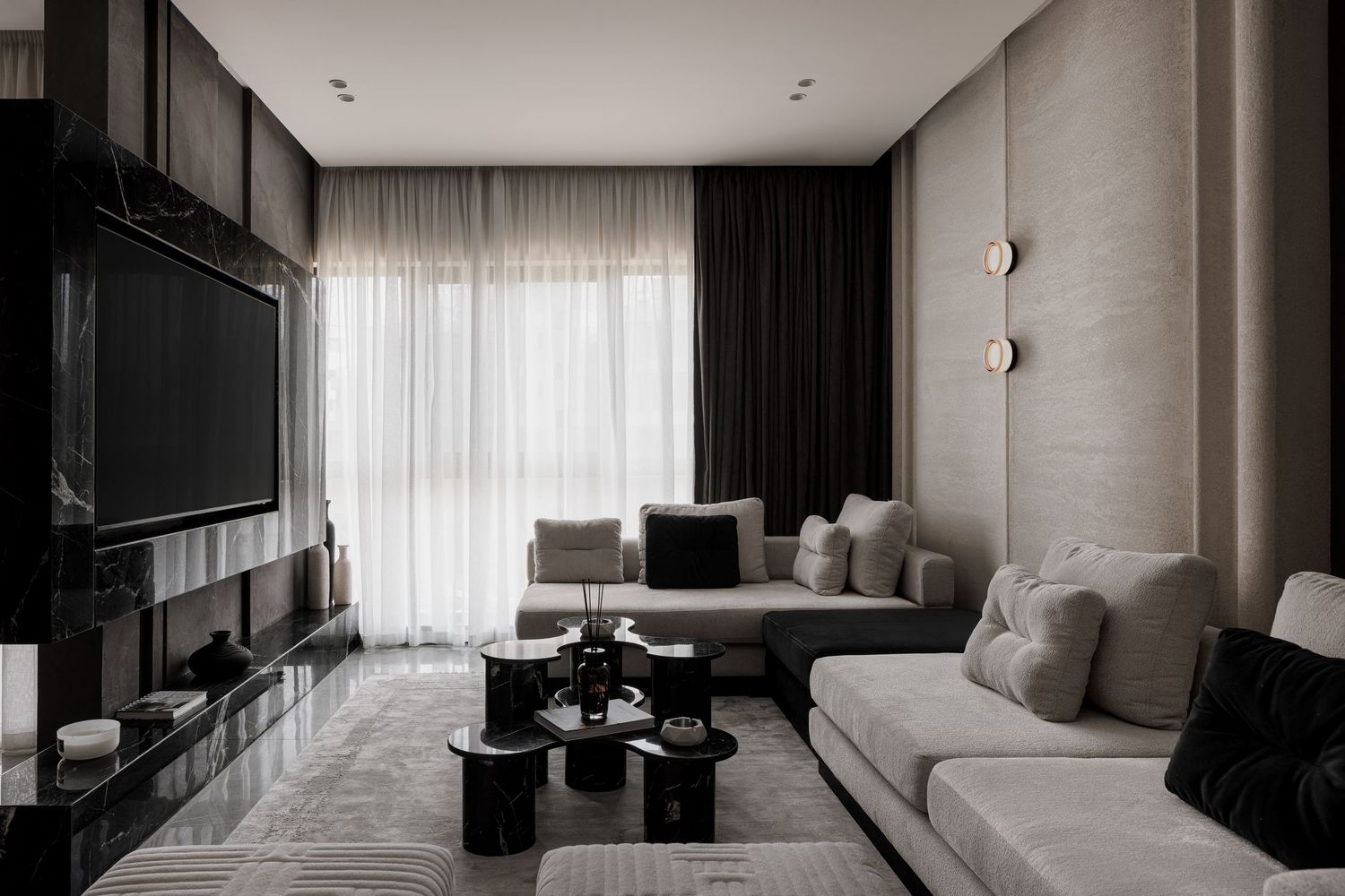 Elegant modern living room with large grey sofa, black coffee tables, wall-mounted TV, and soft ambient lighting.