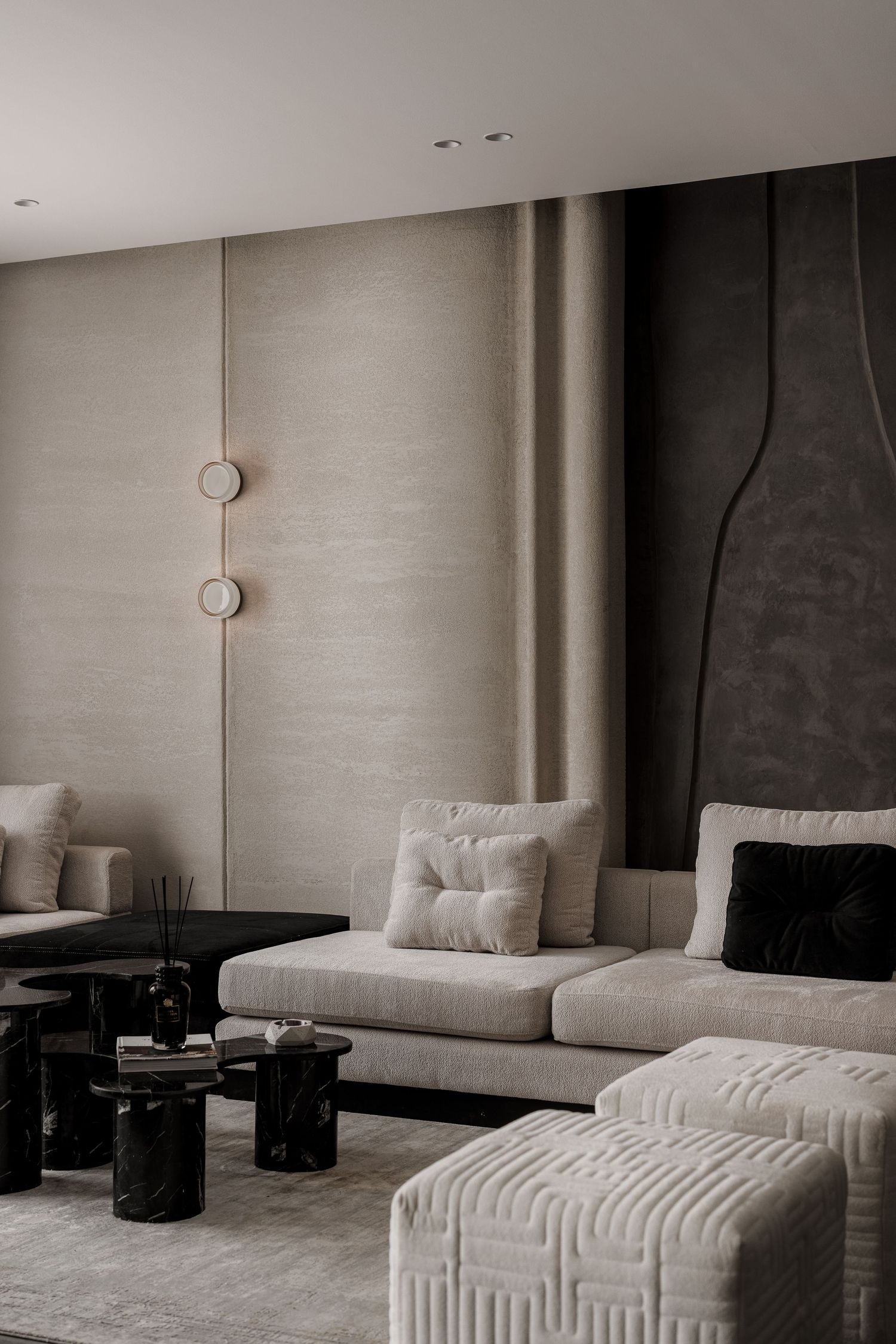 Modern living room detail with beige sectional sofa, black marble side tables, and layered textured wall panels.