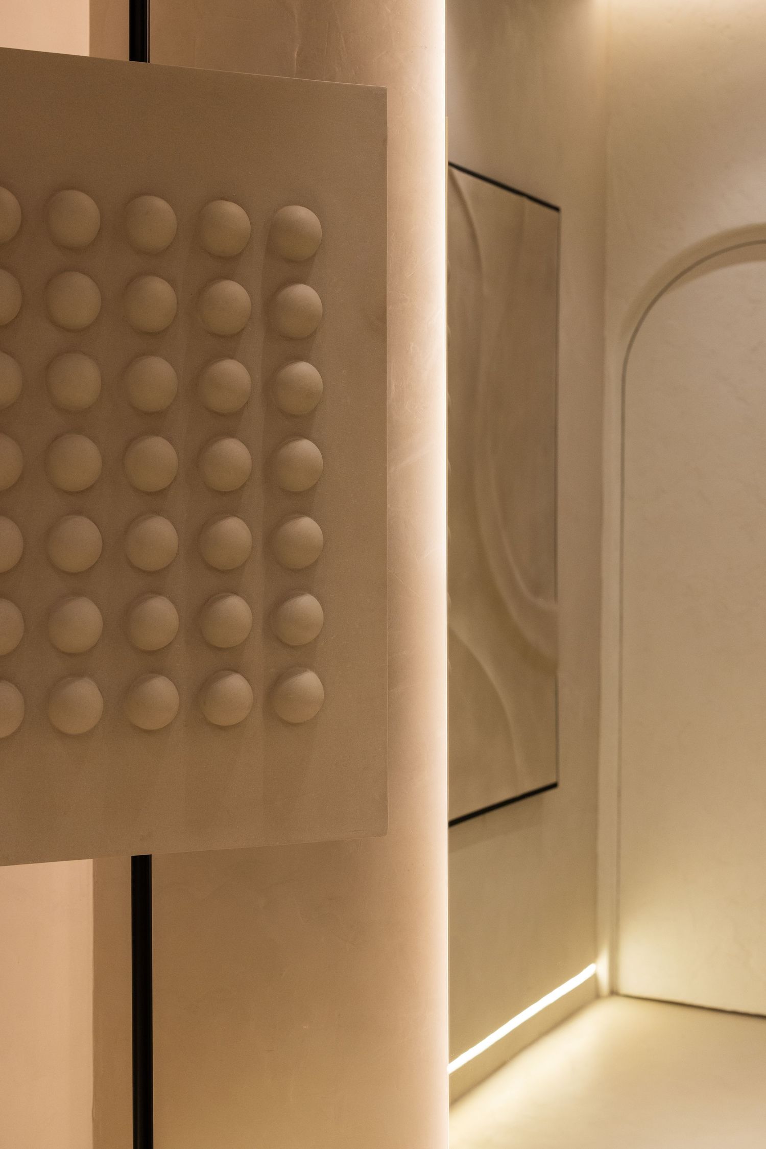 Warm-lit corridor with embossed dot-pattern panel, glowing strip lighting, arched doorway, and sculptural wall relief artwork.