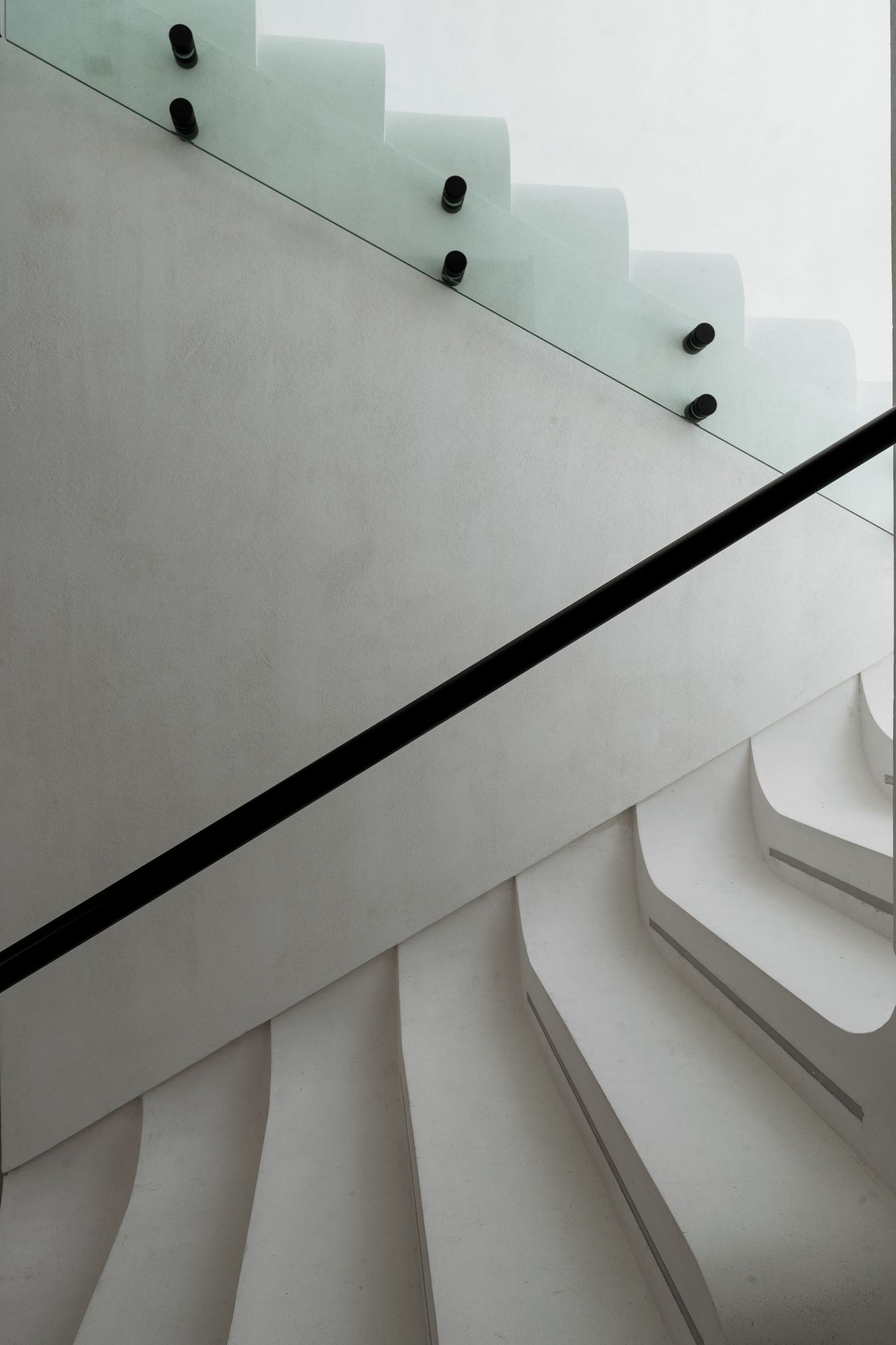 Modern white spiral staircase with glass railing and black hardware, viewed from below in minimalist interior.