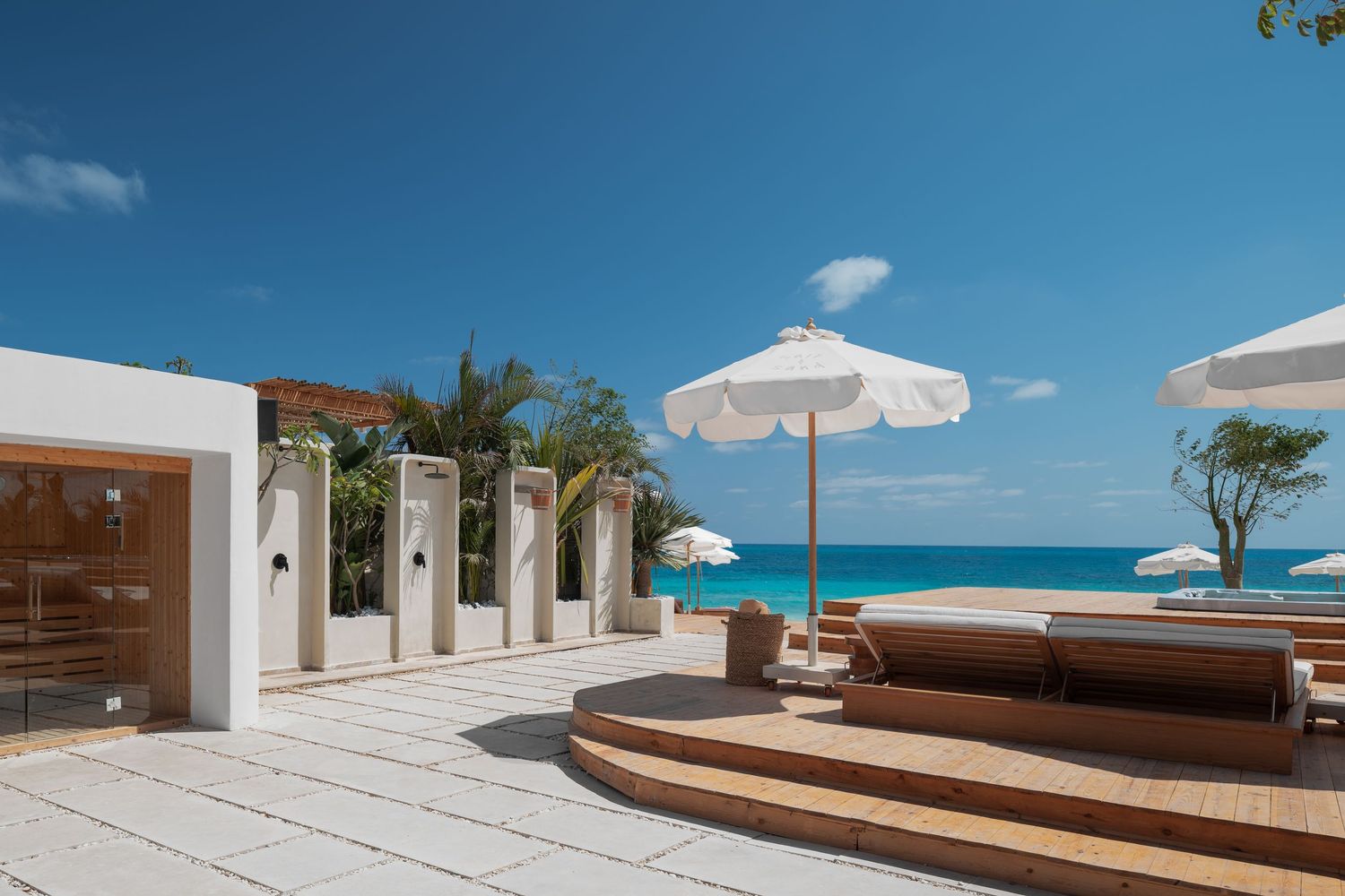 Stunning beachfront terrace with sun loungers, white umbrellas, outdoor showers, and turquoise Caribbean sea views.