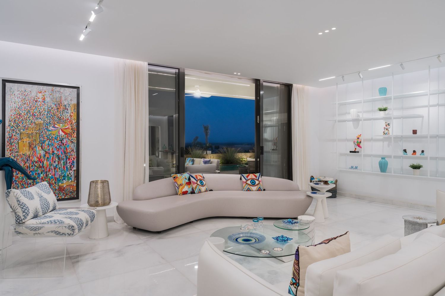 Elegant curved sofa in bright white living room with vibrant artwork and built-in shelving at dusk.