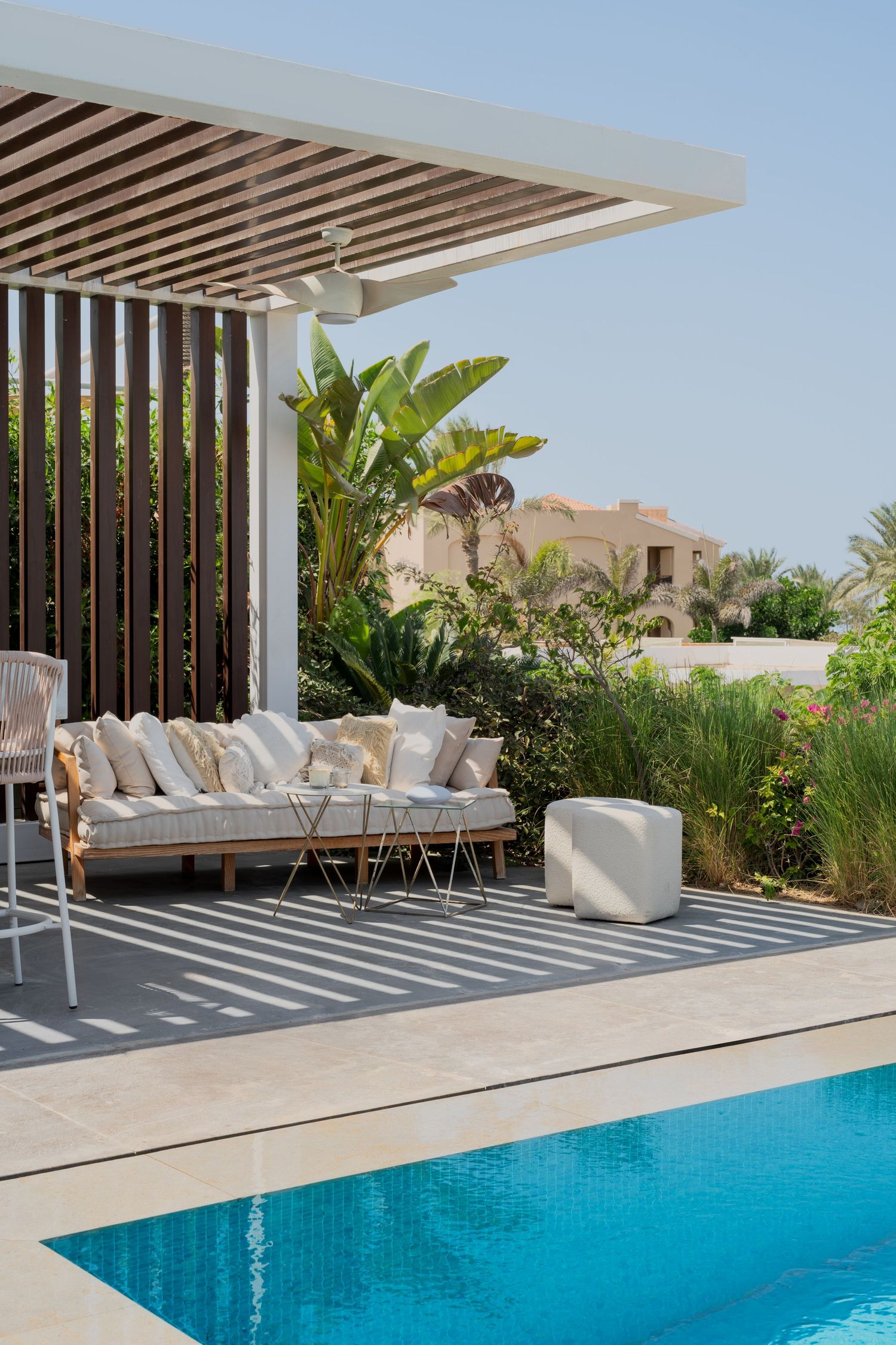 Luxury villa pool area with teak pergola, outdoor sofa with cushions, tropical garden, and clear blue swimming pool.