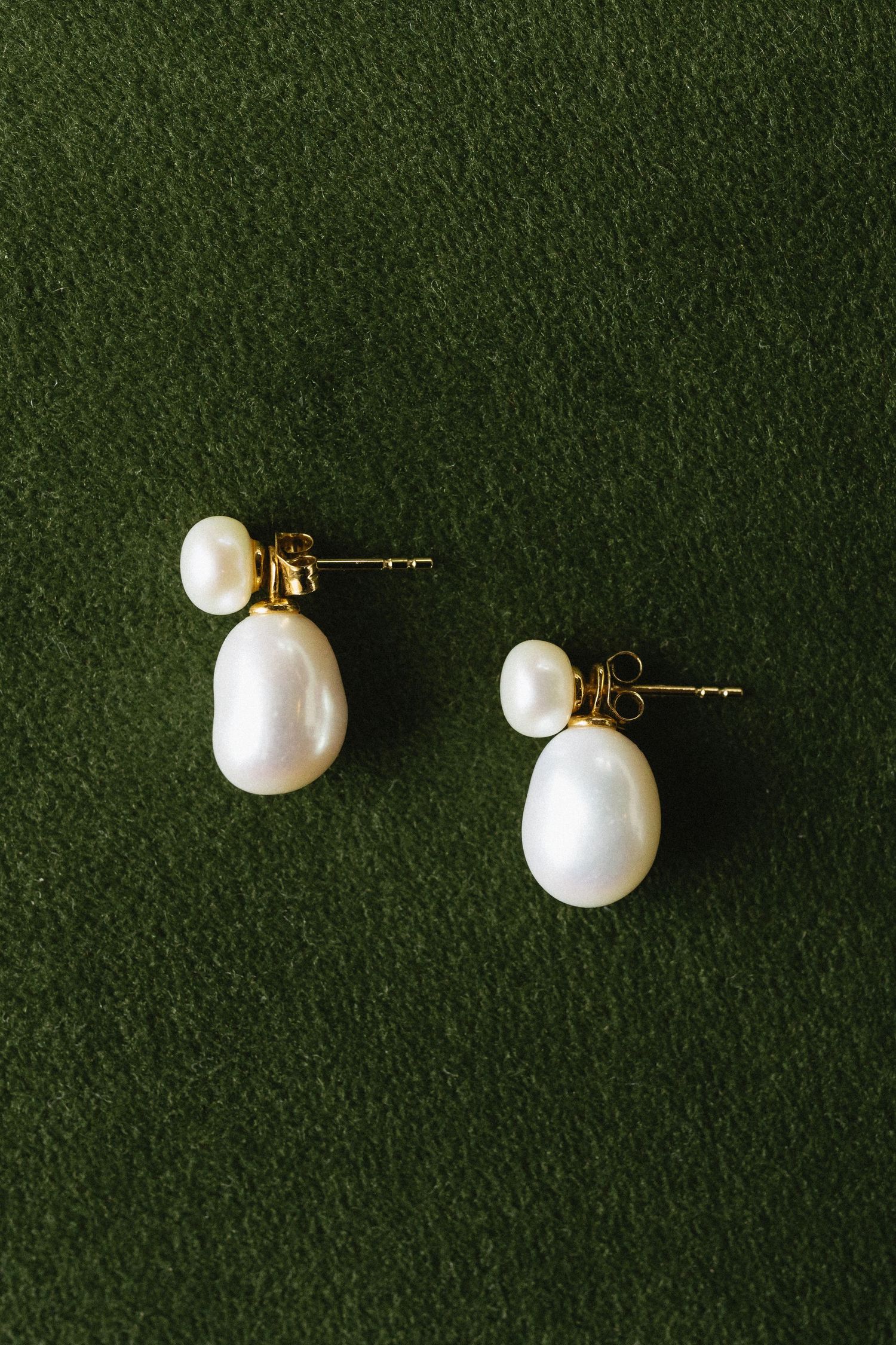 Pearl stud earrings with gold posts displayed on dark green velvet background in multiple angles.