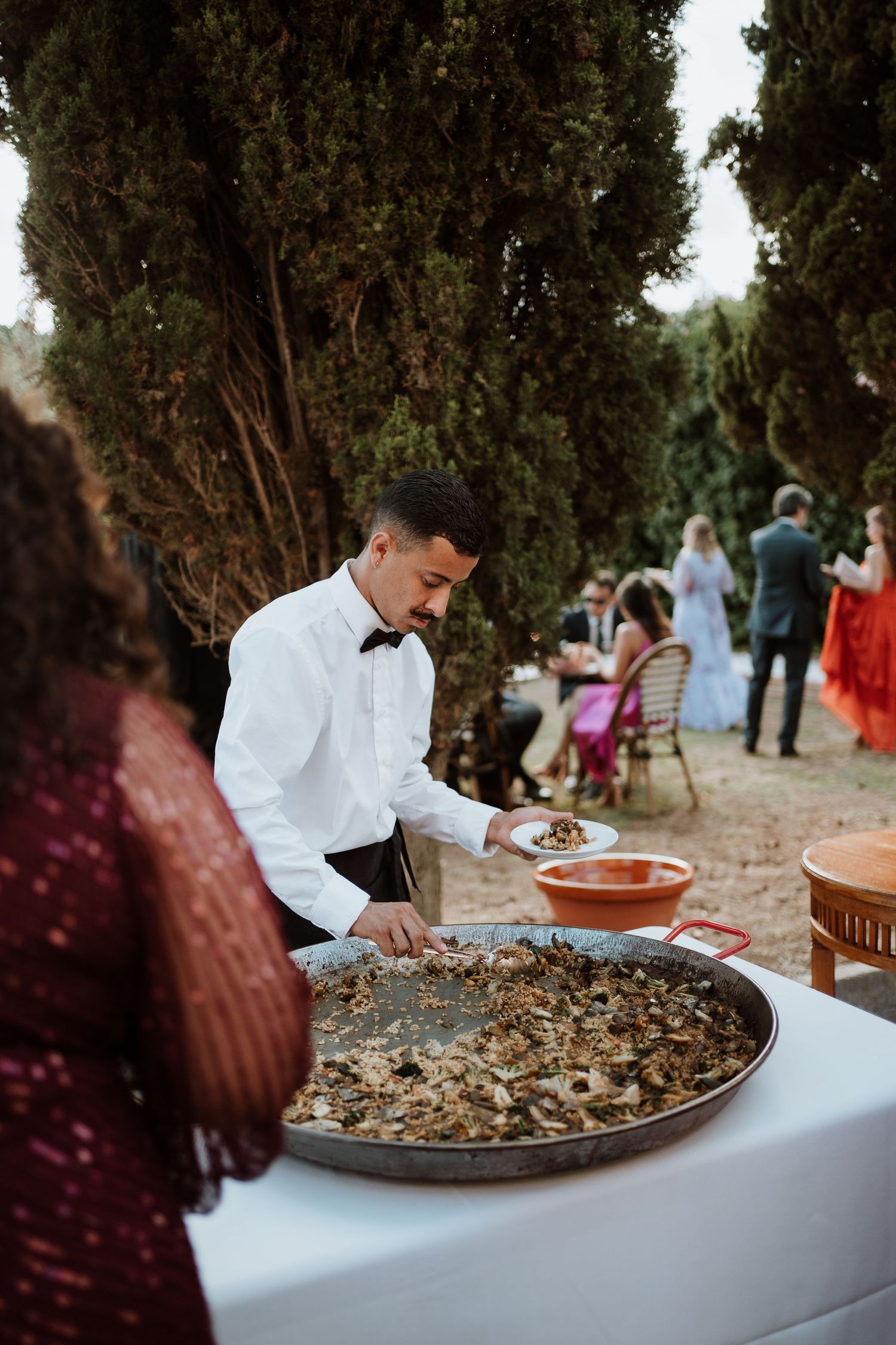 Catering staff preparing large paella dish at outdoor wedding reception with cypress trees in Barcelona at gran villa rosa.