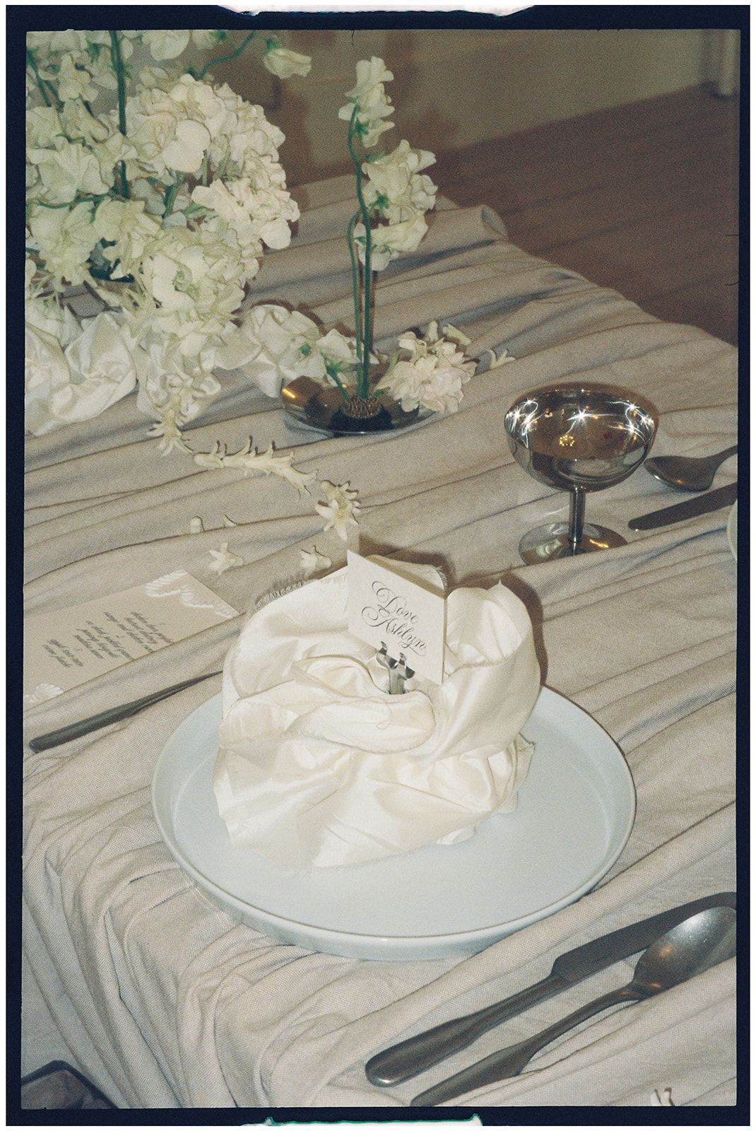 White meringue dessert with flower decorations sits on a plate atop a textured tablecloth.
