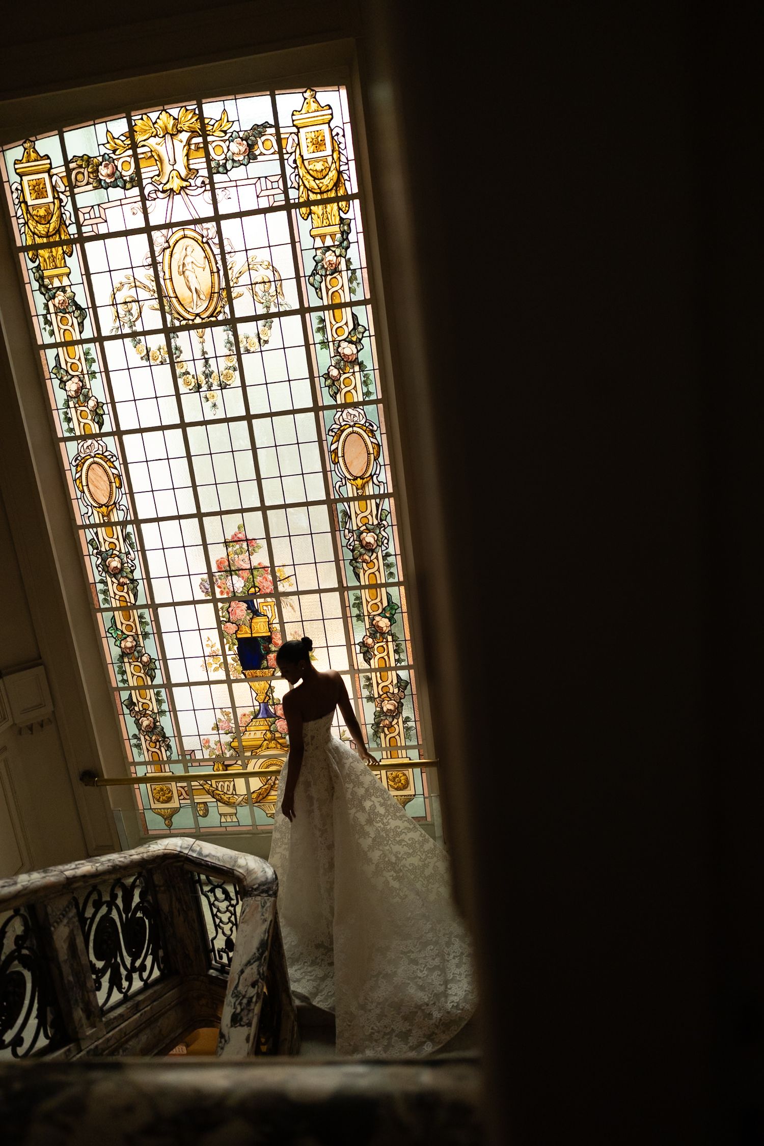 A silhouetted figure stands by an ornate stained glass window on a staircase, creating a dramatic backlit composition.
