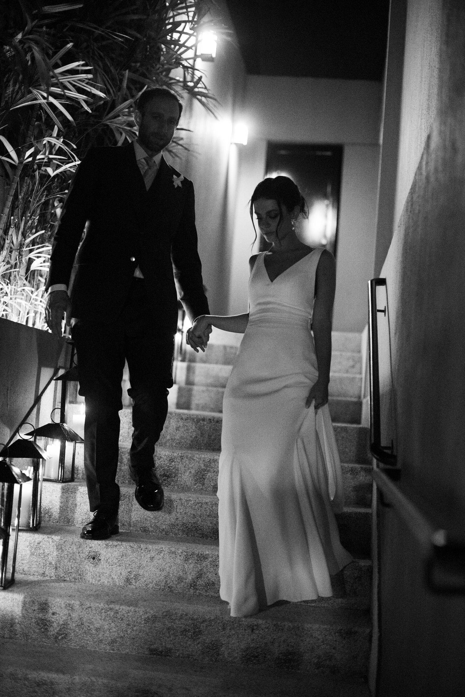 A dramatic black and white wedding photograph of a couple descending stone steps at night with elegant evening attire.