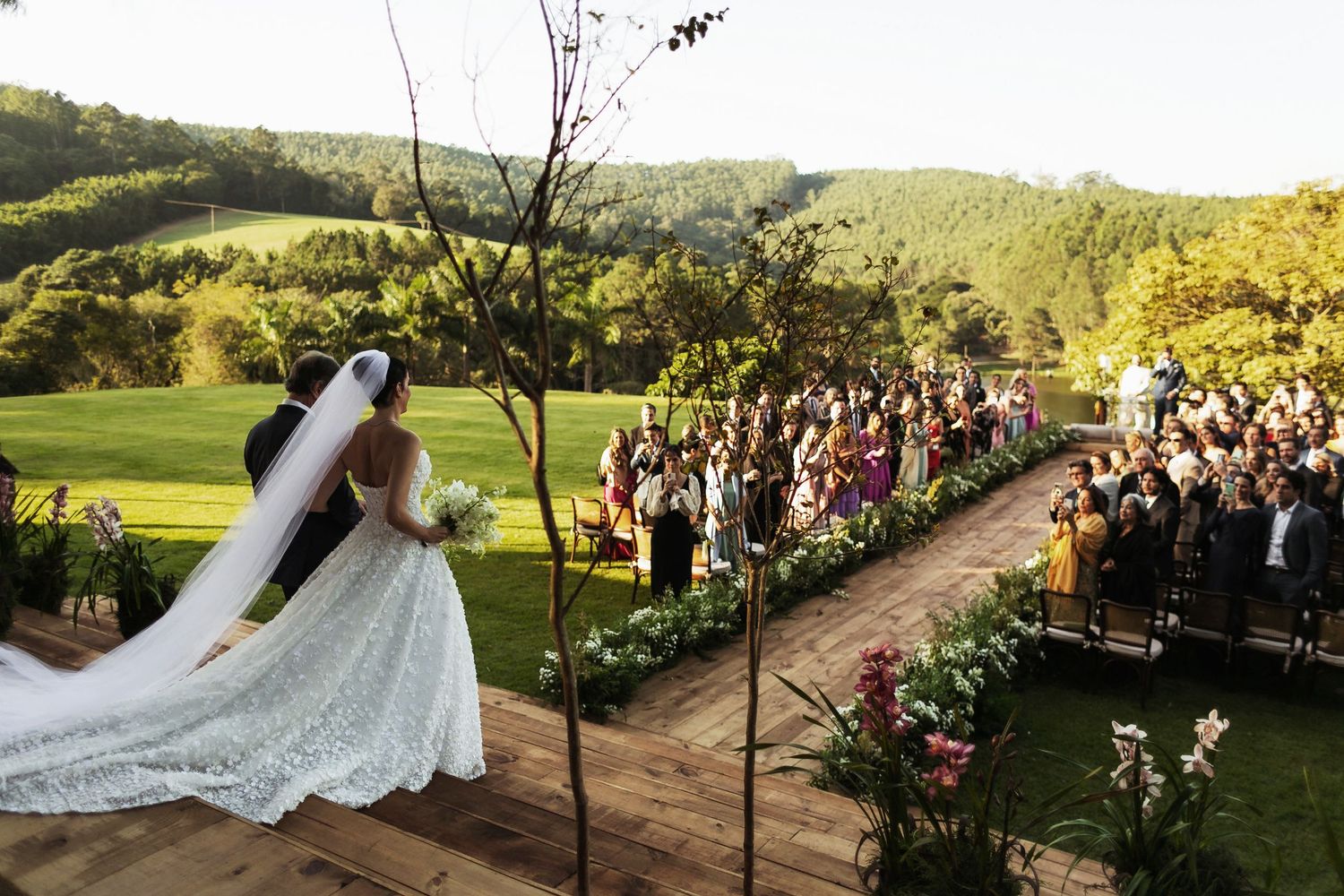 A beautiful outdoor vineyard wedding ceremony setup with rolling hills and lush greenery in the background at sunset.