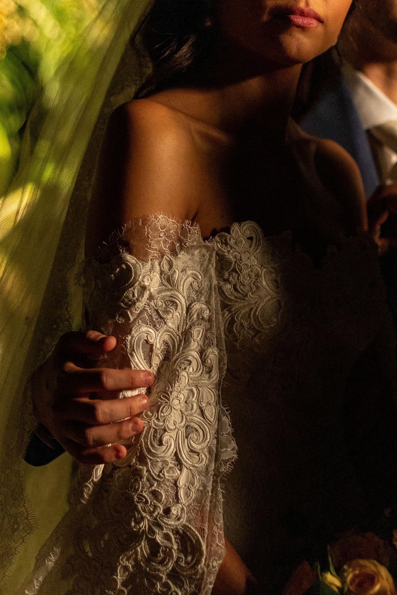 Artistic close-up of intricate white lace wedding dress details in dramatic lighting with shadows and green tones.