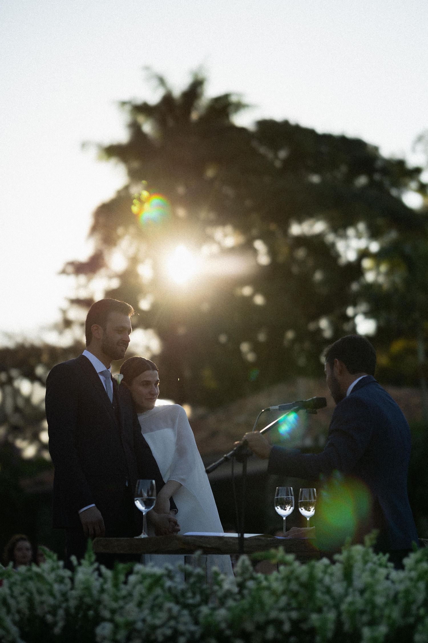 A romantic outdoor dinner scene at sunset with glowing light flares and silhouettes against a darkening sky.