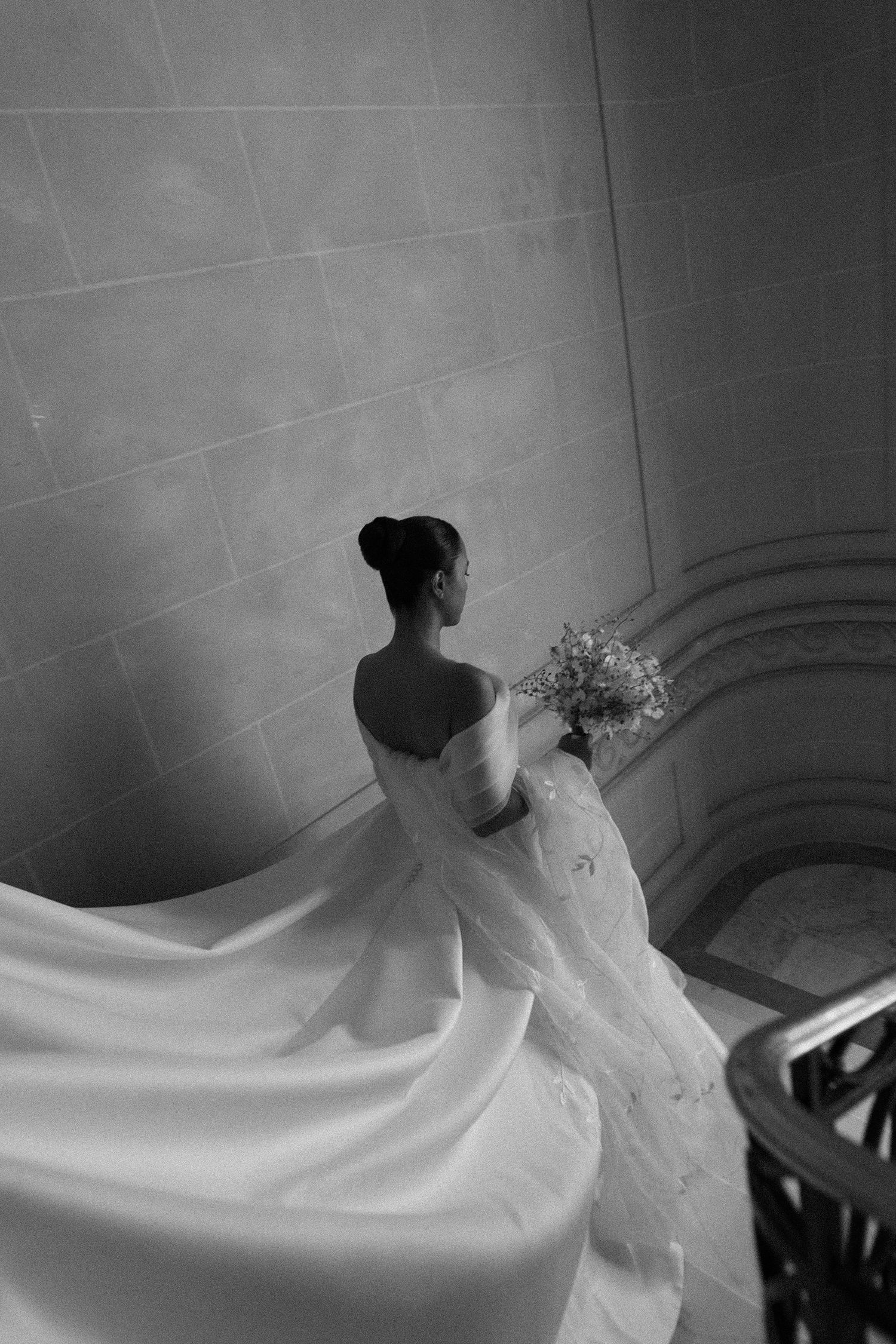 A flowing white wedding dress with delicate details captured in a dramatic black and white photograph series.