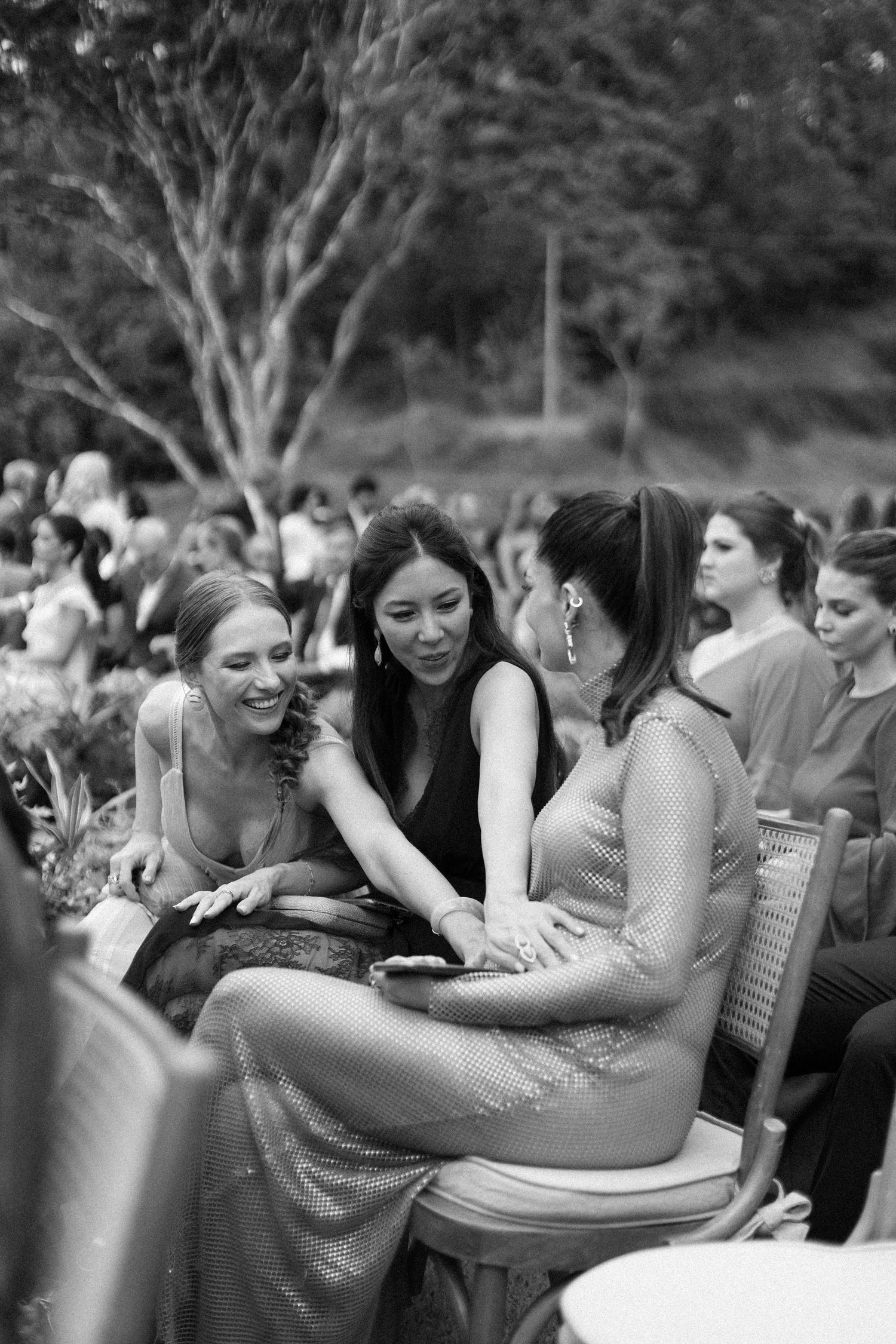 A group of friends laughing and enjoying conversation while sitting together outdoors in black and white.