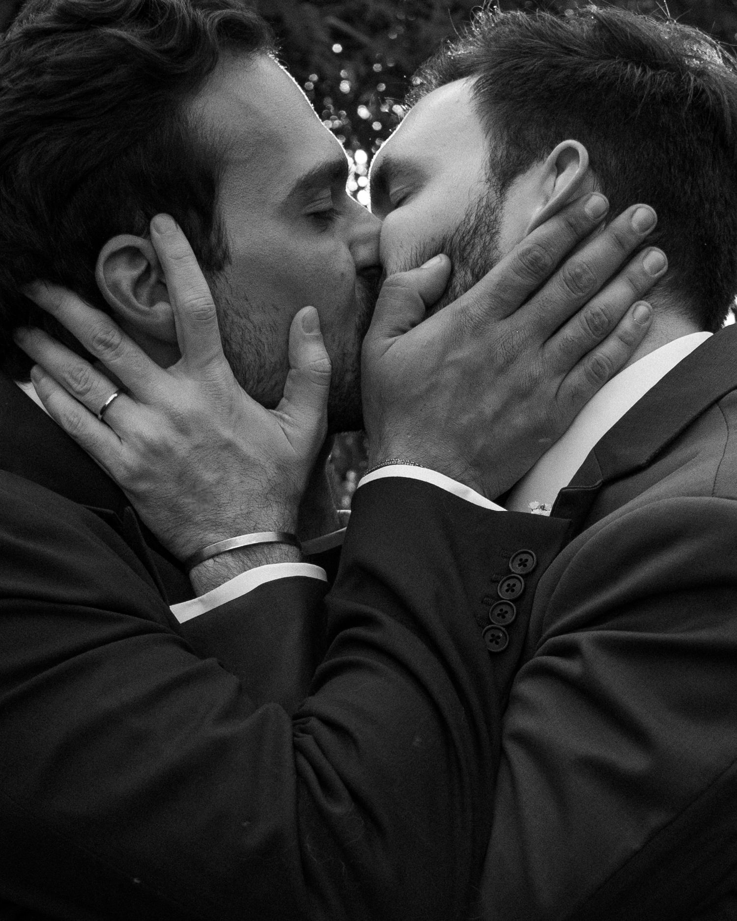 A tender black and white photograph of a romantic kiss between two people in formal suits.