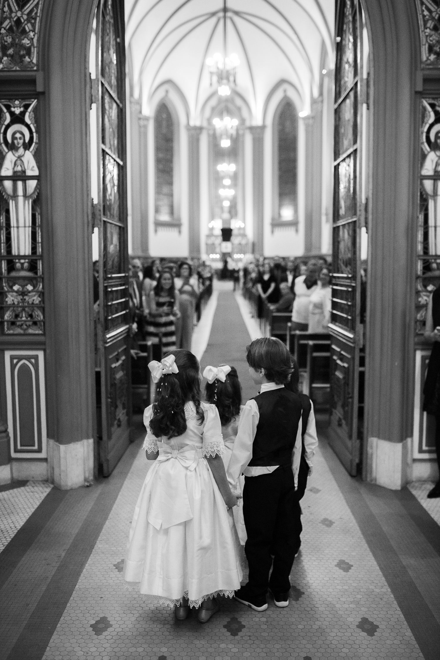 Children in formal attire standing at entrance of gothic church during wedding ceremony.