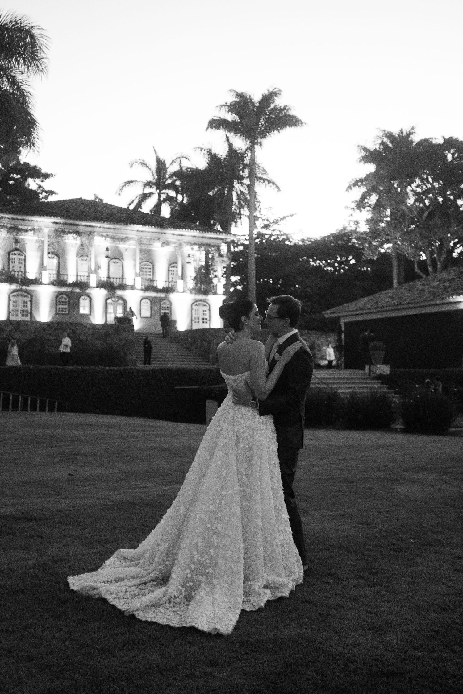 A romantic black and white wedding photo of a couple dancing on a lawn in front of an elegant colonial mansion.