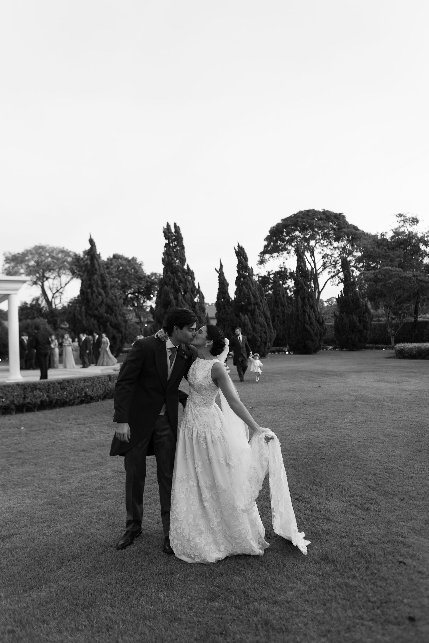 Black and white wedding photography sequence shows a couple and their attendants walking across a grassy outdoor venue.