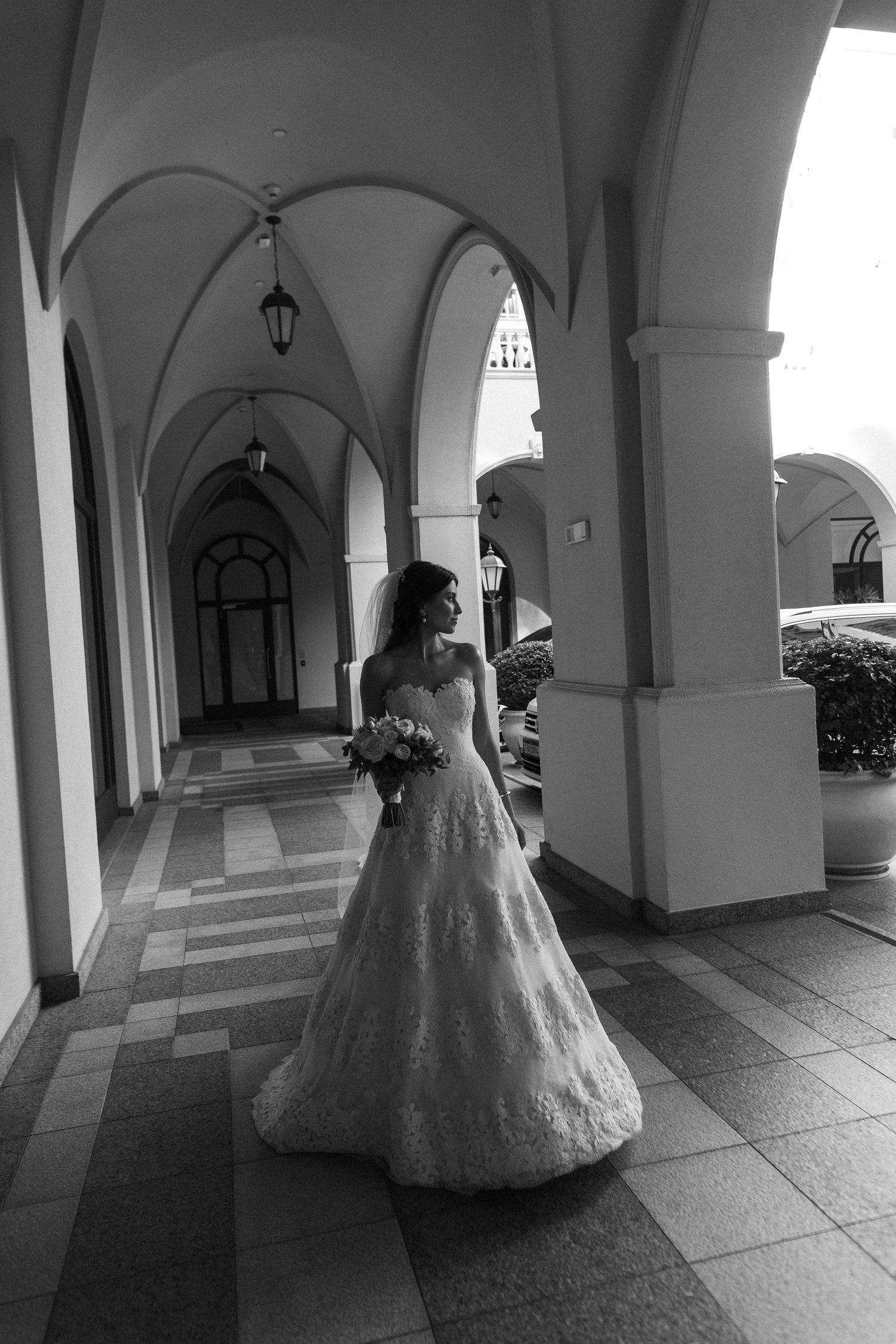 A sequence of black and white photos showing a person in an elegant ball gown walking through an arched colonnade.