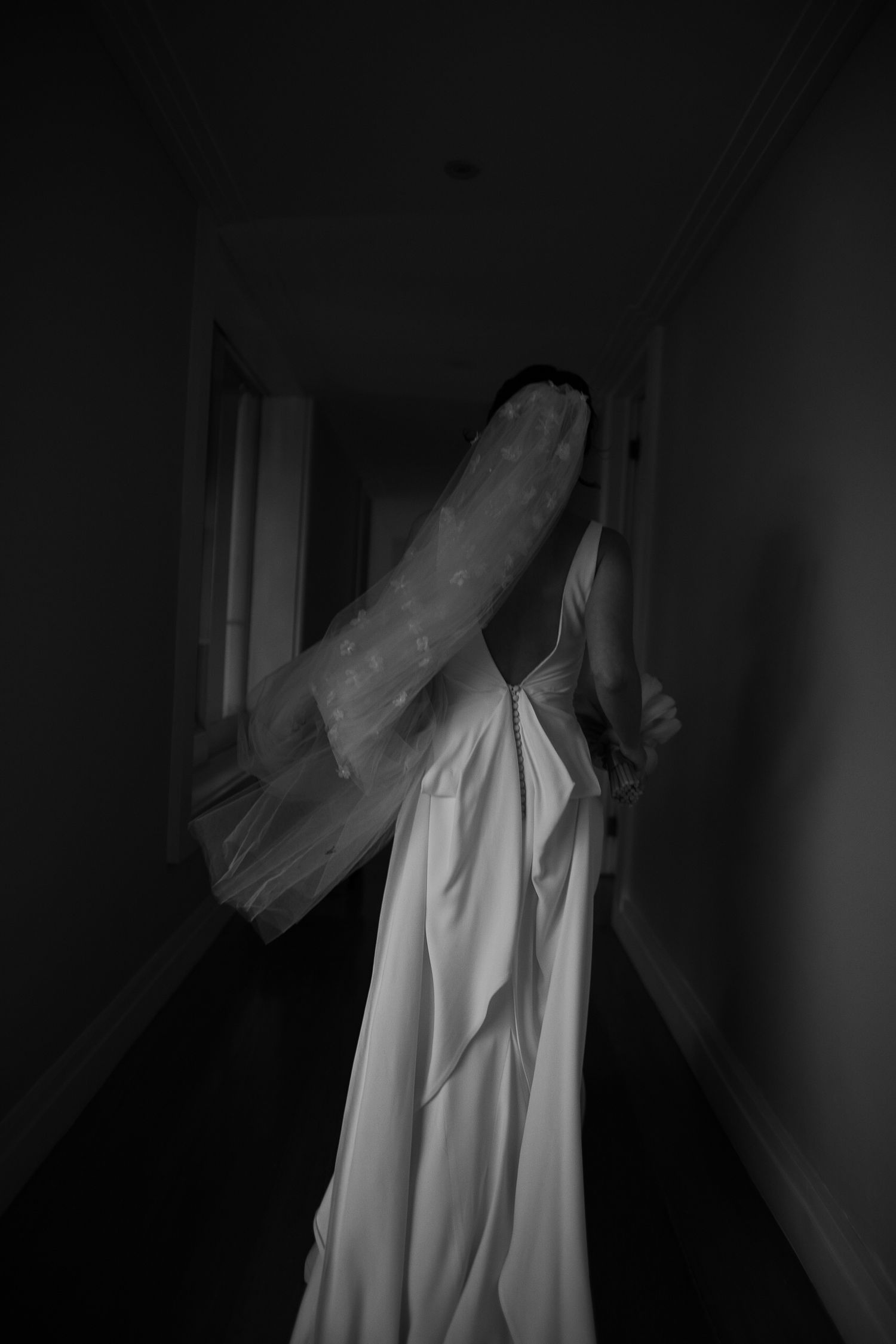 Artistic black and white photo of a wedding dress silhouette in a dark hallway.