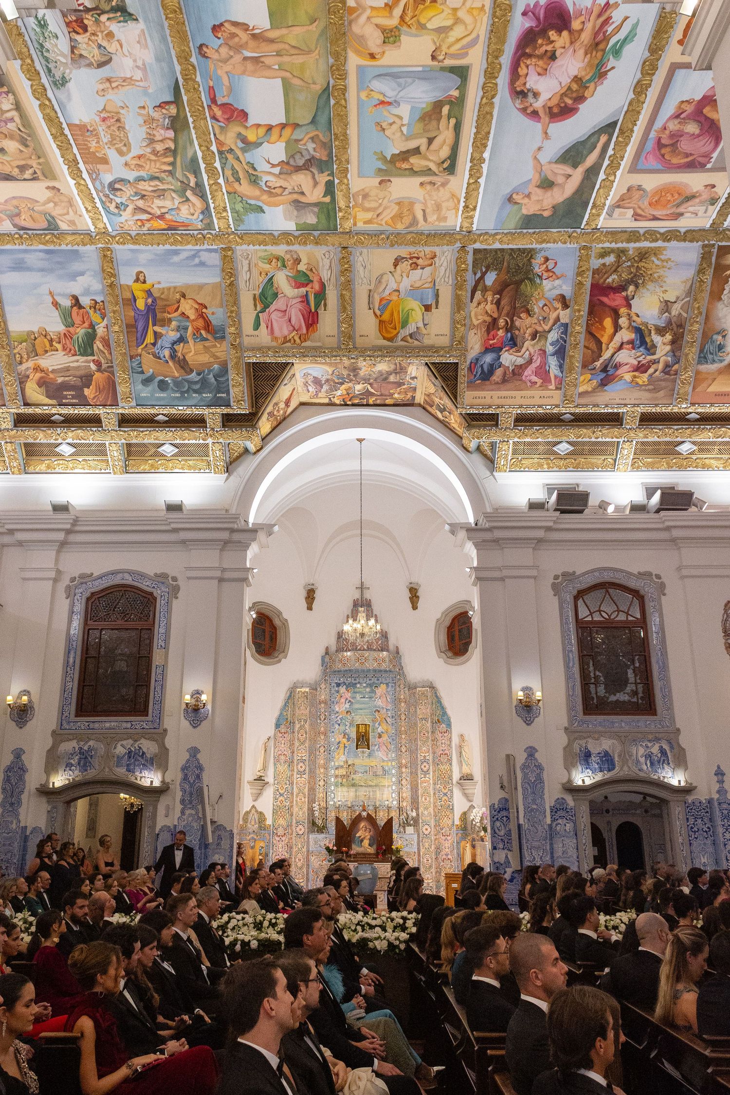Elegant ballroom with ornate frescoed ceiling and chandeliers hosts a formal gathering of guests in evening attire.
