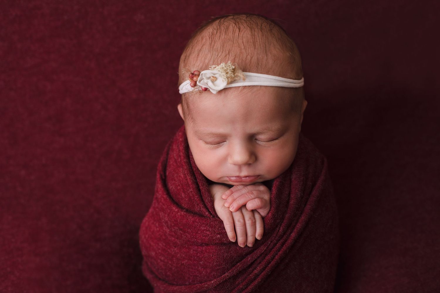 Pasgeboren baby met wit haarbandje geposeerd met hoofdje leunend op handjes