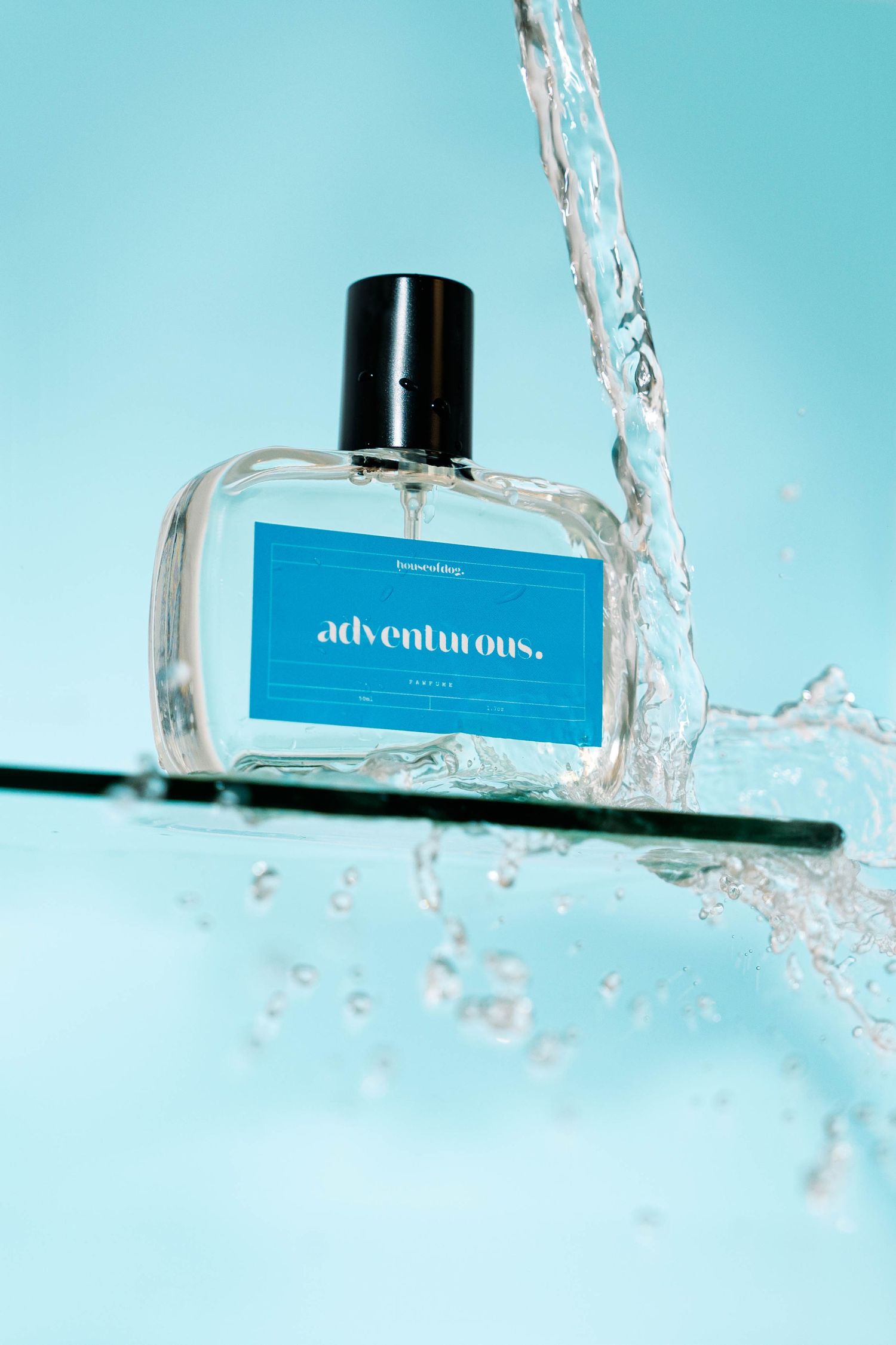 A glass perfume bottle labeled 'adventurous' with splashing water against a turquoise background.
