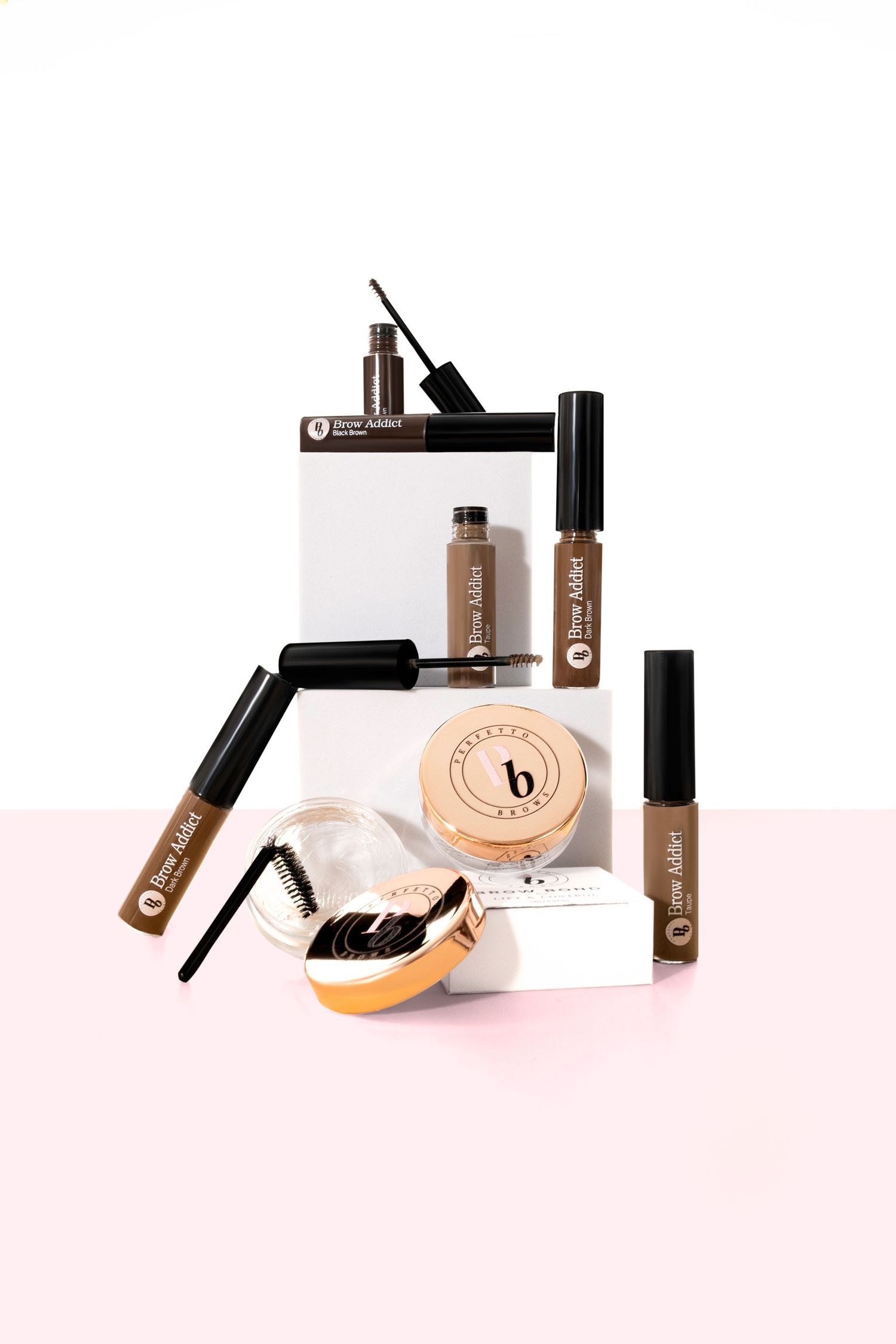 Beauty products including mascara, foundation, powder, and brushes arranged on a pink and white background.