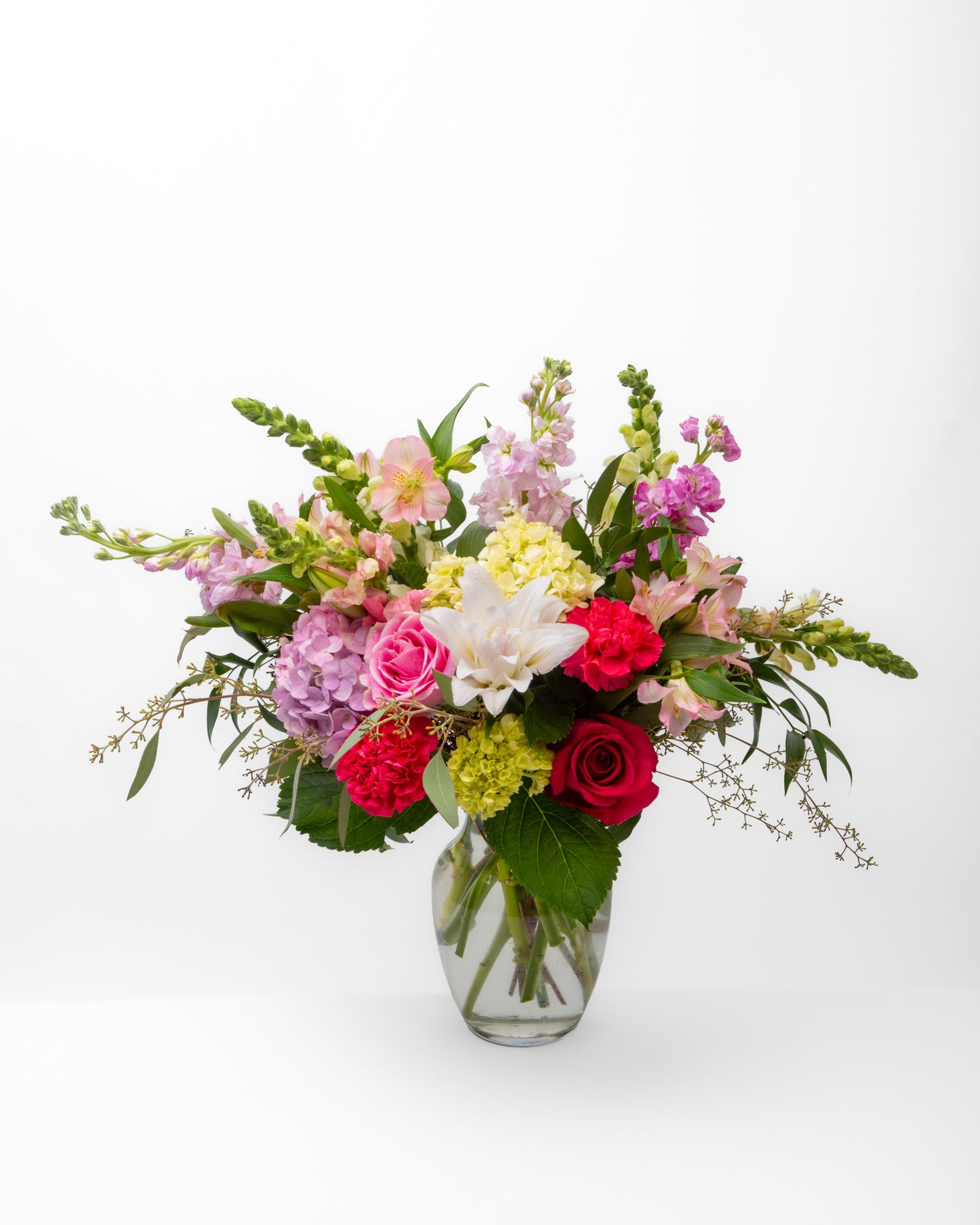 Colorful flower arrangement including roses and lilies in a glass vase.