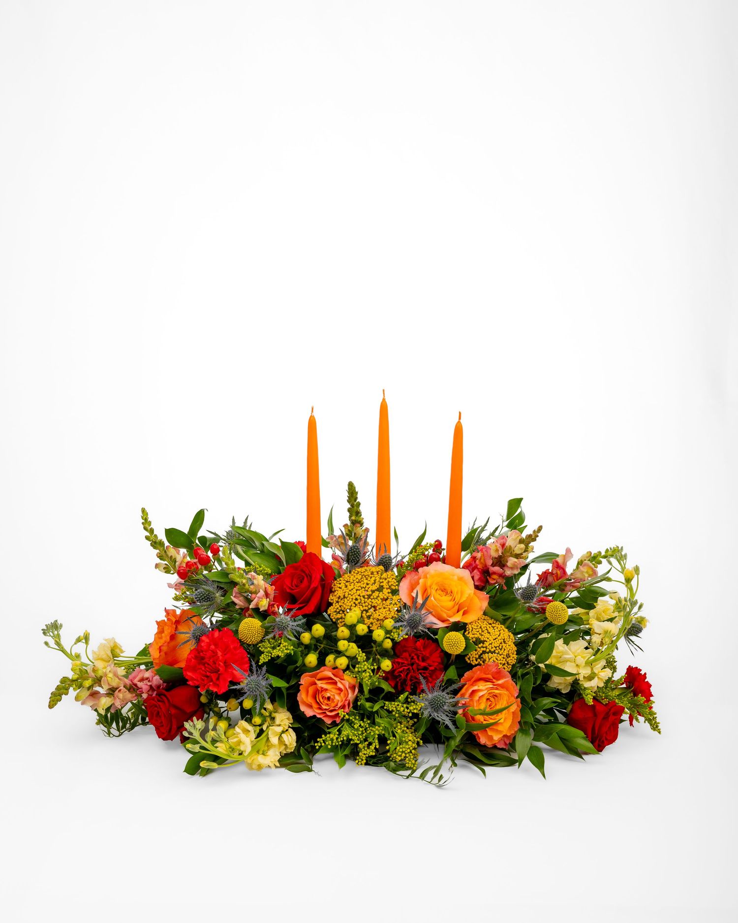 Large flower arrangement in fall colors with three orange candles on a white background.
