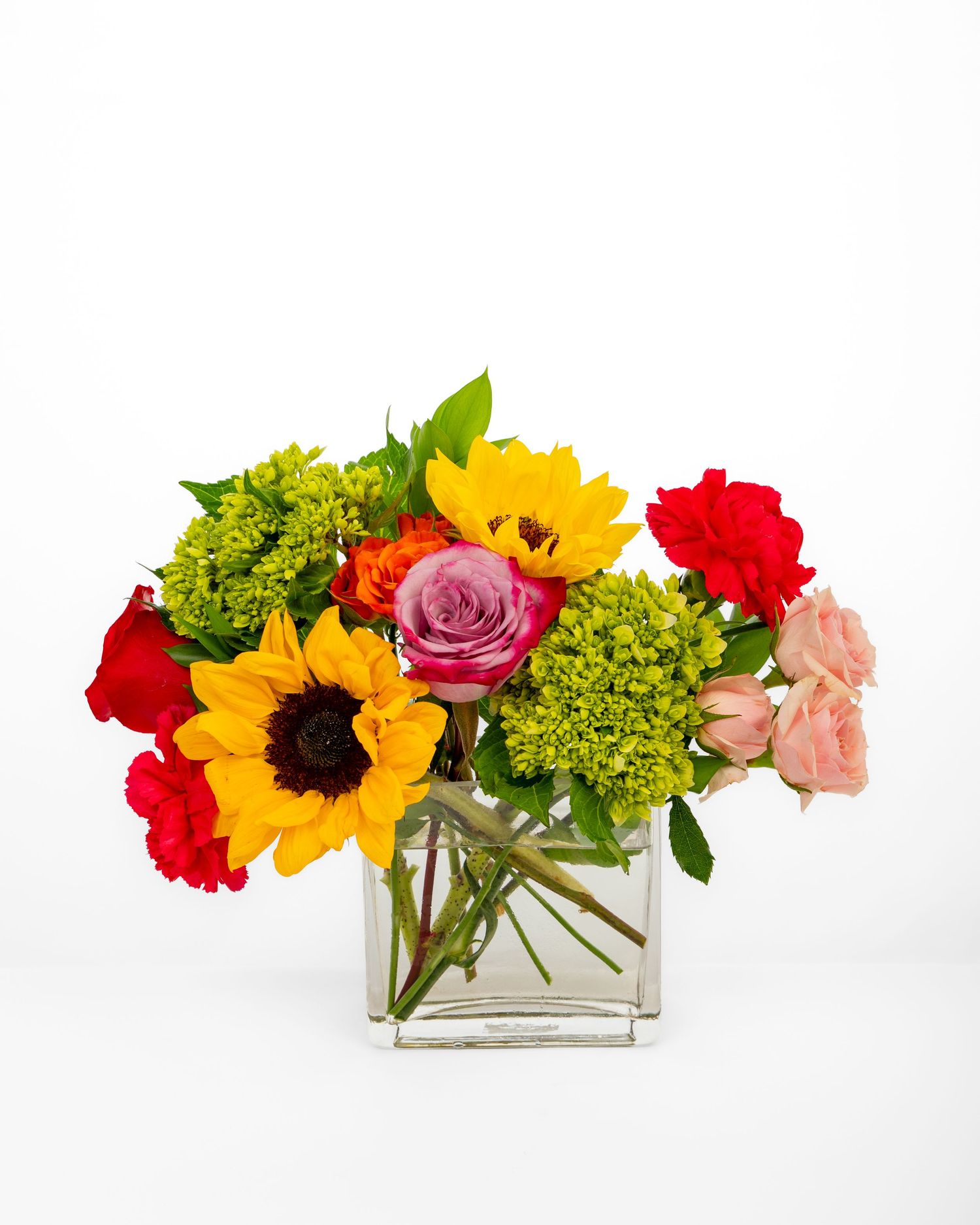 Fresh flower arrangement with sunflowers, roses, and hydrangeas in a clear square glass vase.