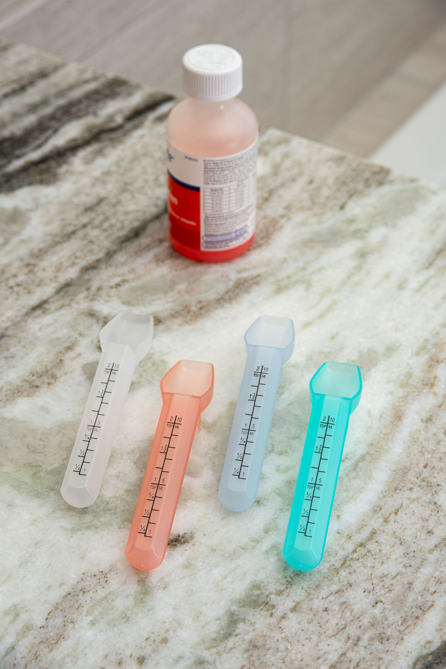 Product shot of four liquid medicine dispenser spoons on a counter with a bottle of liquid medicine.