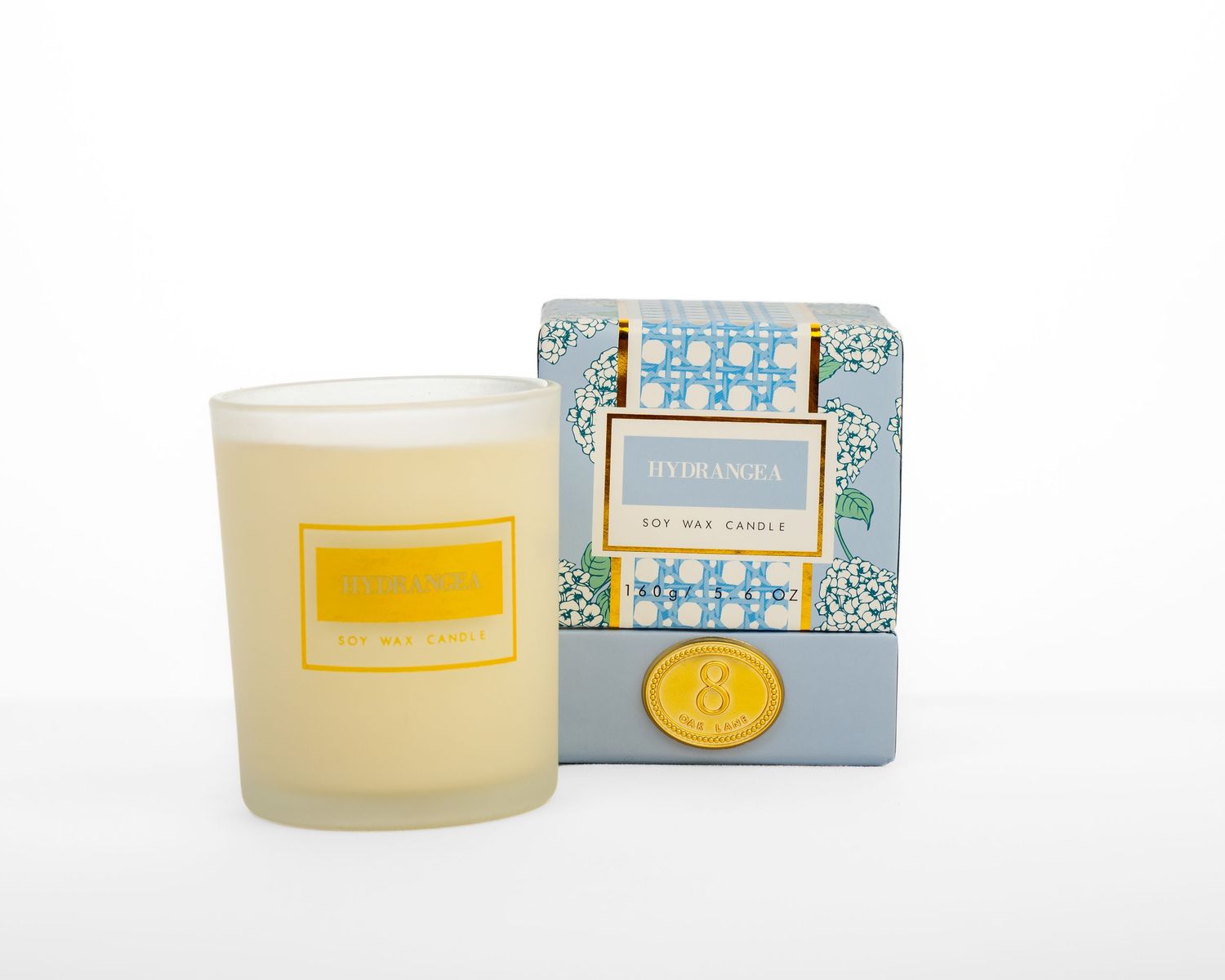 White candle in a glass cup with a decorative blue gift box.