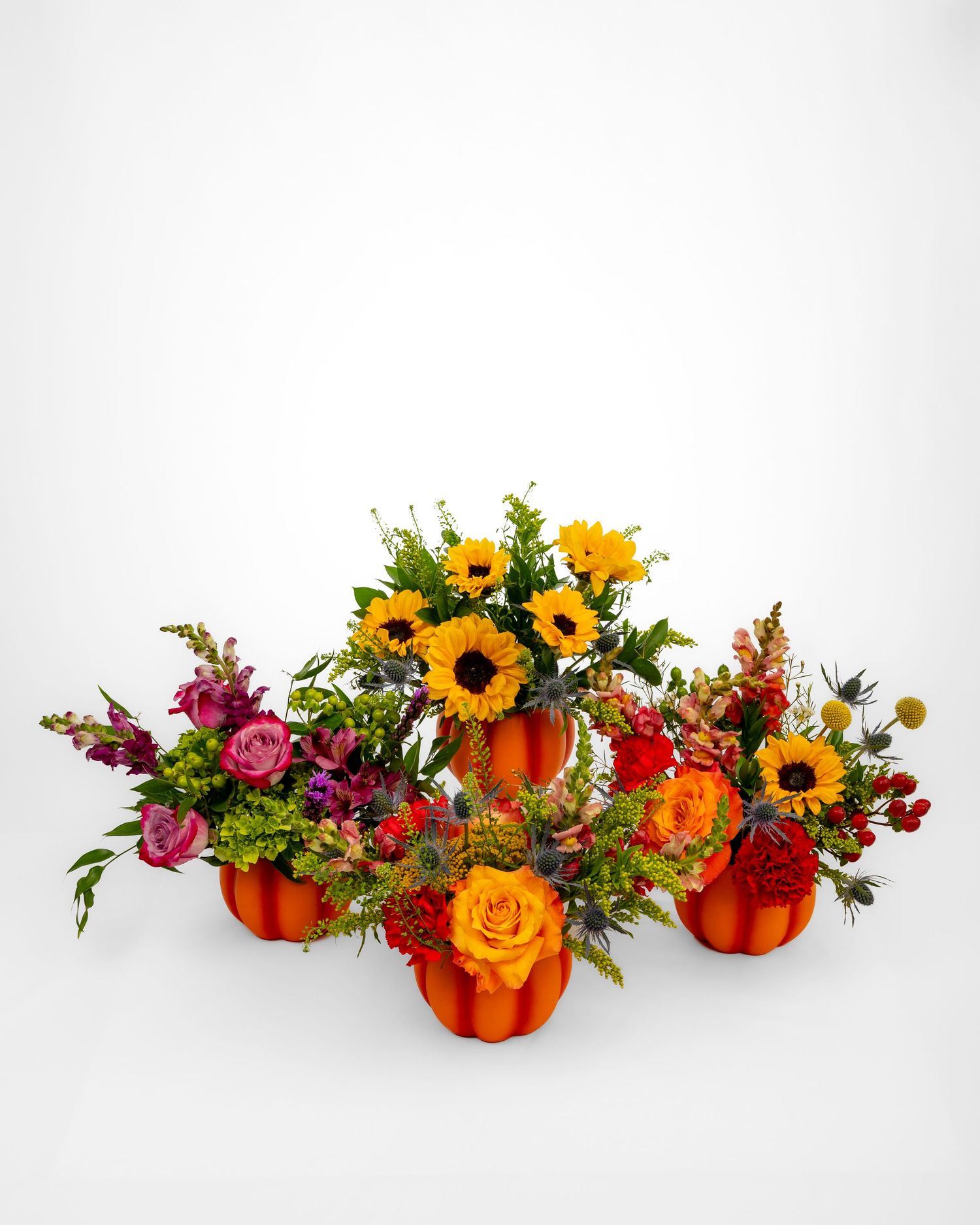 Four flower arrangements in pumpkin vases, all in fall colors.