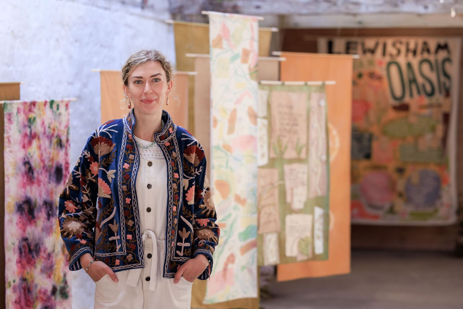 Blonde haired young women standing surrounded by colourful naturally dyed textile wallhangings