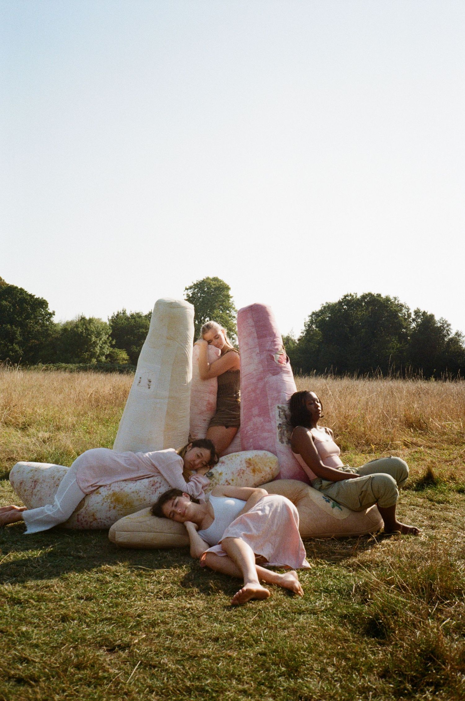 four women with different ethnicities sitting and resting on colourful textile boulders outside in a meadow