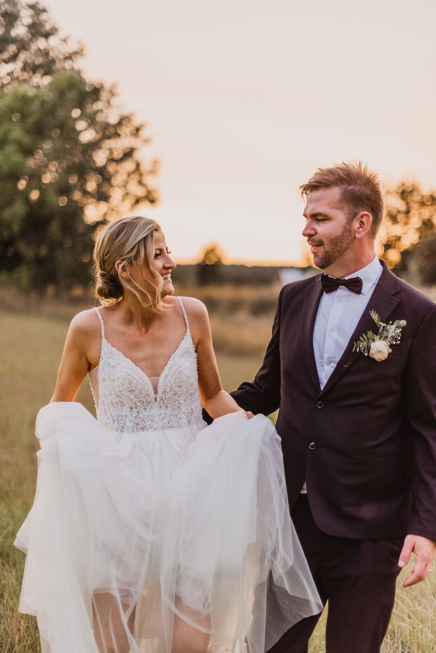 A joyful couple shares candid moments in a golden field at sunset wearing wedding attire.