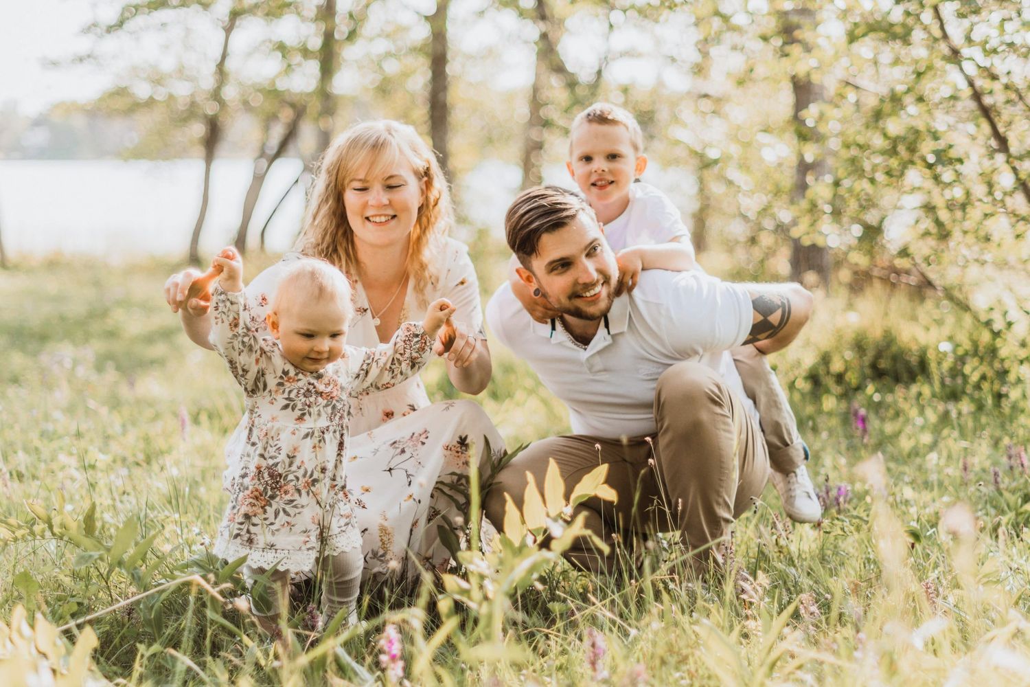 Happy family with two young children sitting in a sunny green meadow surrounded by trees.