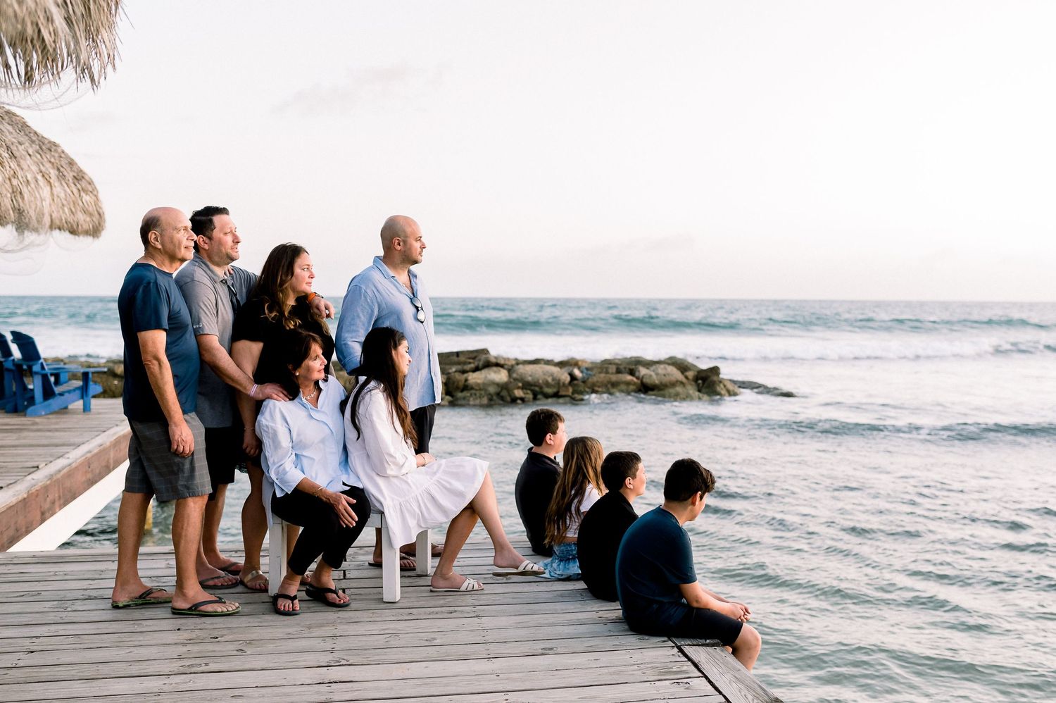 Family group posing on a wooden pier by the ocean at sunset, with waves and rocky shoreline in the background.