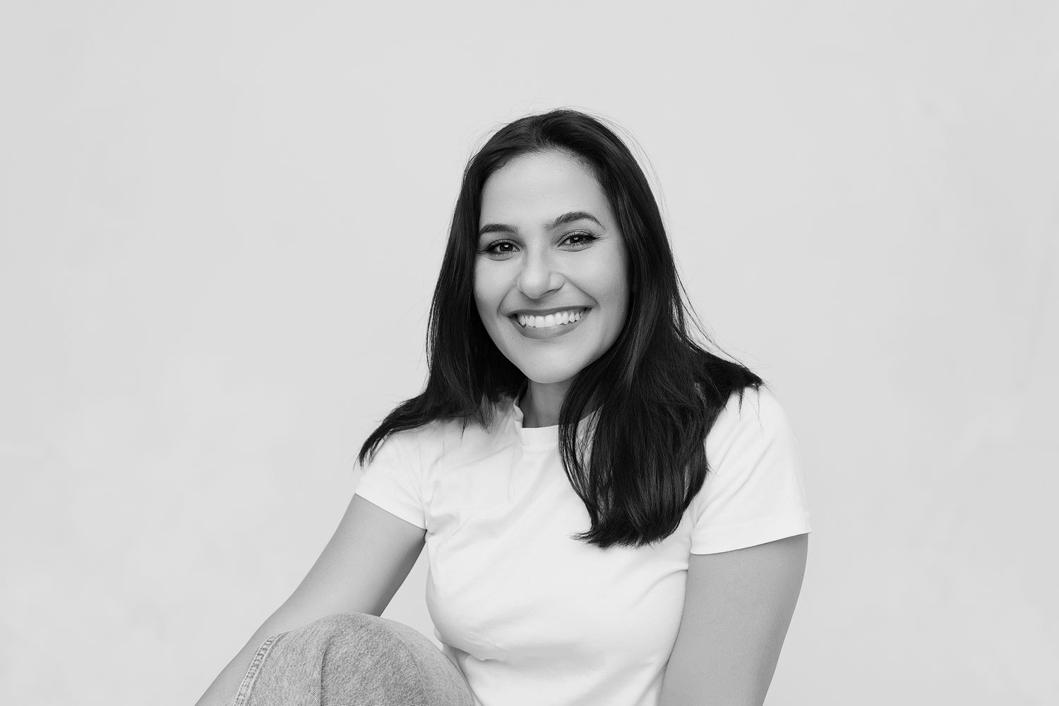 Smiling young woman with dark hair wearing a white t-shirt, posing in a black and white portrait photo.