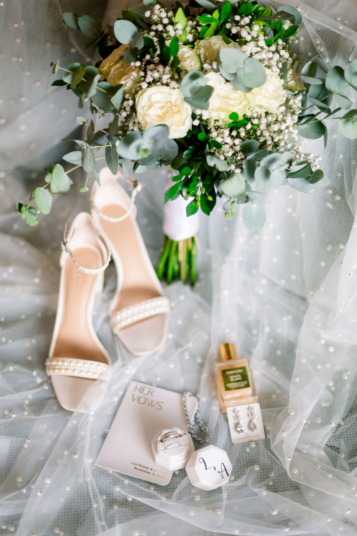 Elegant blush pink wedding shoes displayed with white floral arrangements and delicate tulle fabric.