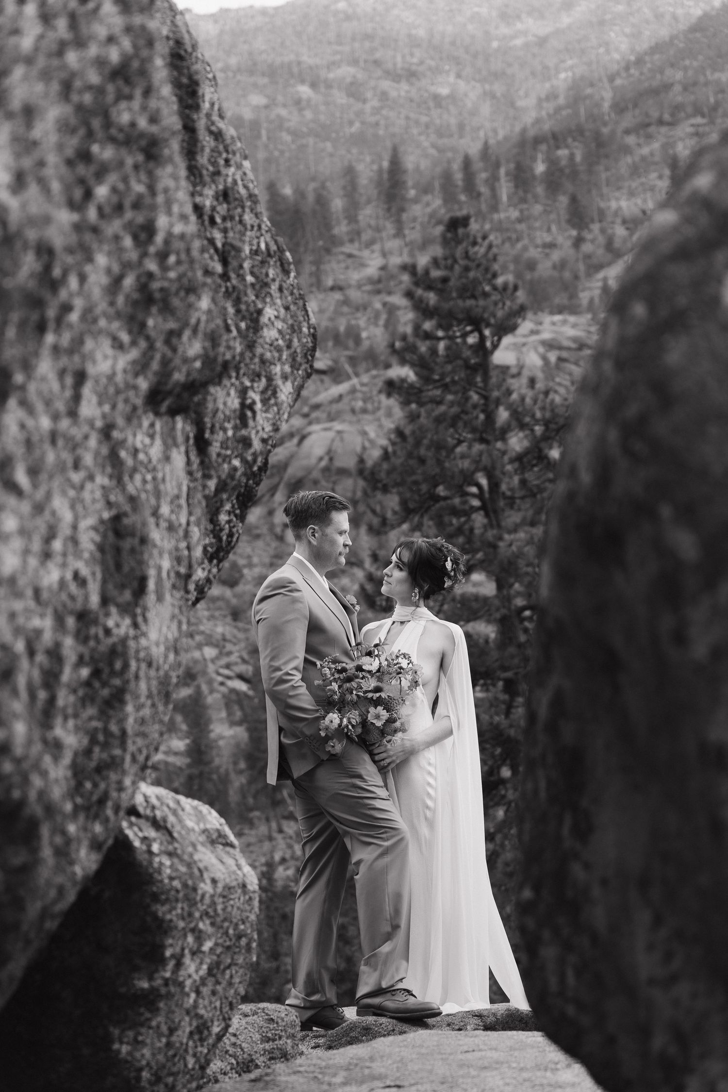 A couple in wedding attire share an intimate moment on a mountain overlook with scenic valley views in the background.