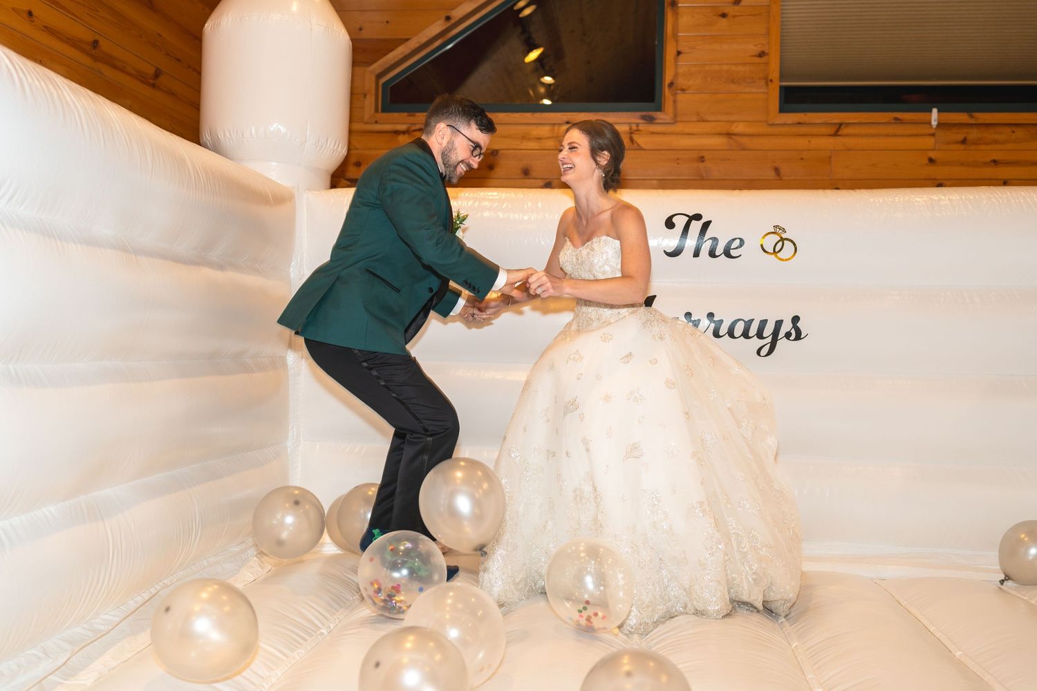 Couple playfully dancing among gold balloons in a rustic wood-paneled wedding venue.